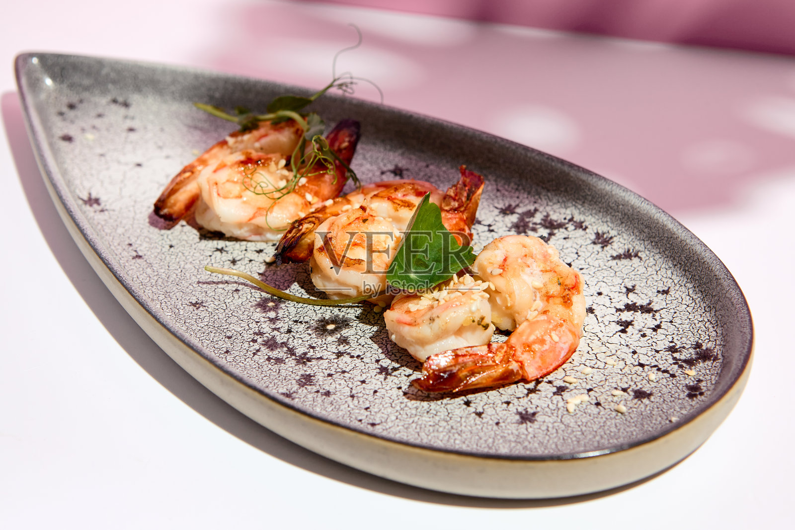 餐厅海鲜-虾烧烤海鲜盘。小菜盘放在白色的桌子上，粉红色的墙壁。白天的阳光和巨大的棕榈叶阴影。夏季或春季的食物概念。照片摄影图片