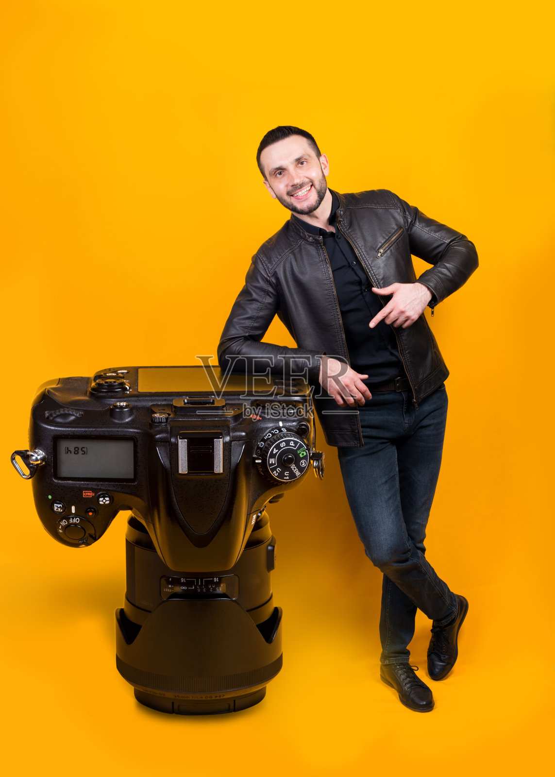 一个笑着的摄影师拿着一个巨大的相机在黄色的背景上照片摄影图片