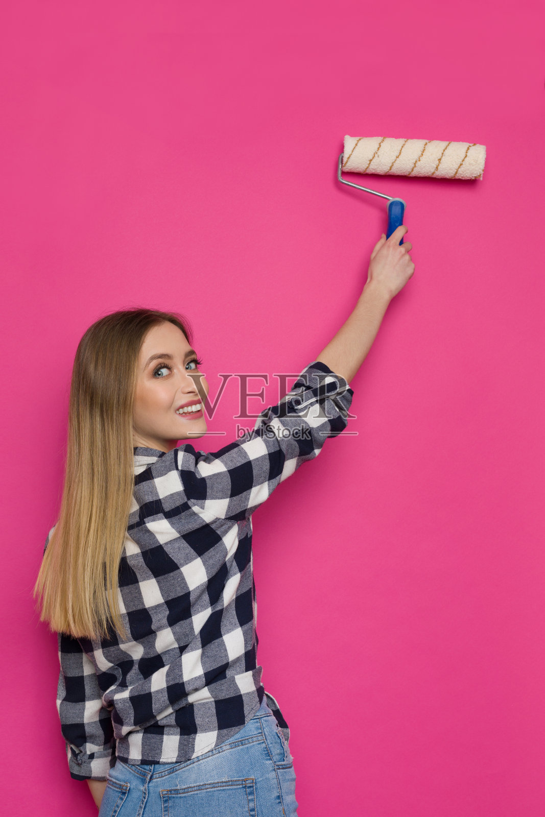 快乐的年轻女人正在刷粉红色的墙照片摄影图片