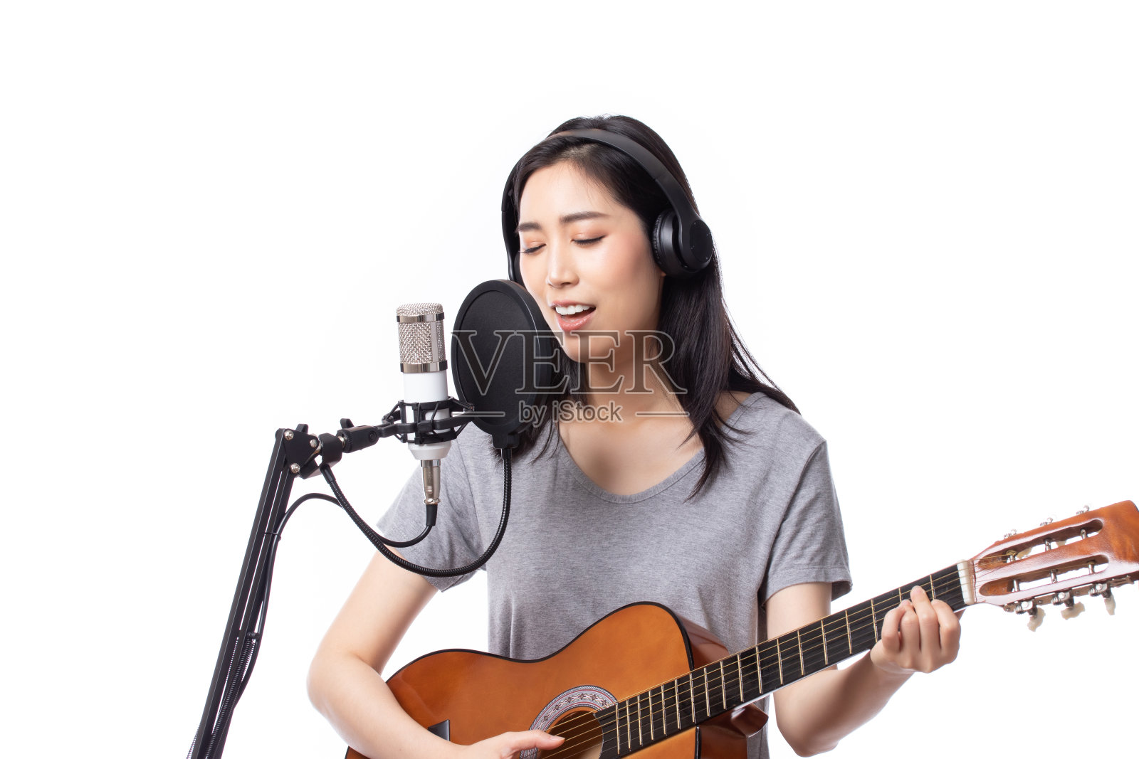 年轻的亚洲女子与麦克风录音歌曲和弹吉他在音乐工作室，女子表演在录音室为她的专辑孤立的白色背景。照片摄影图片