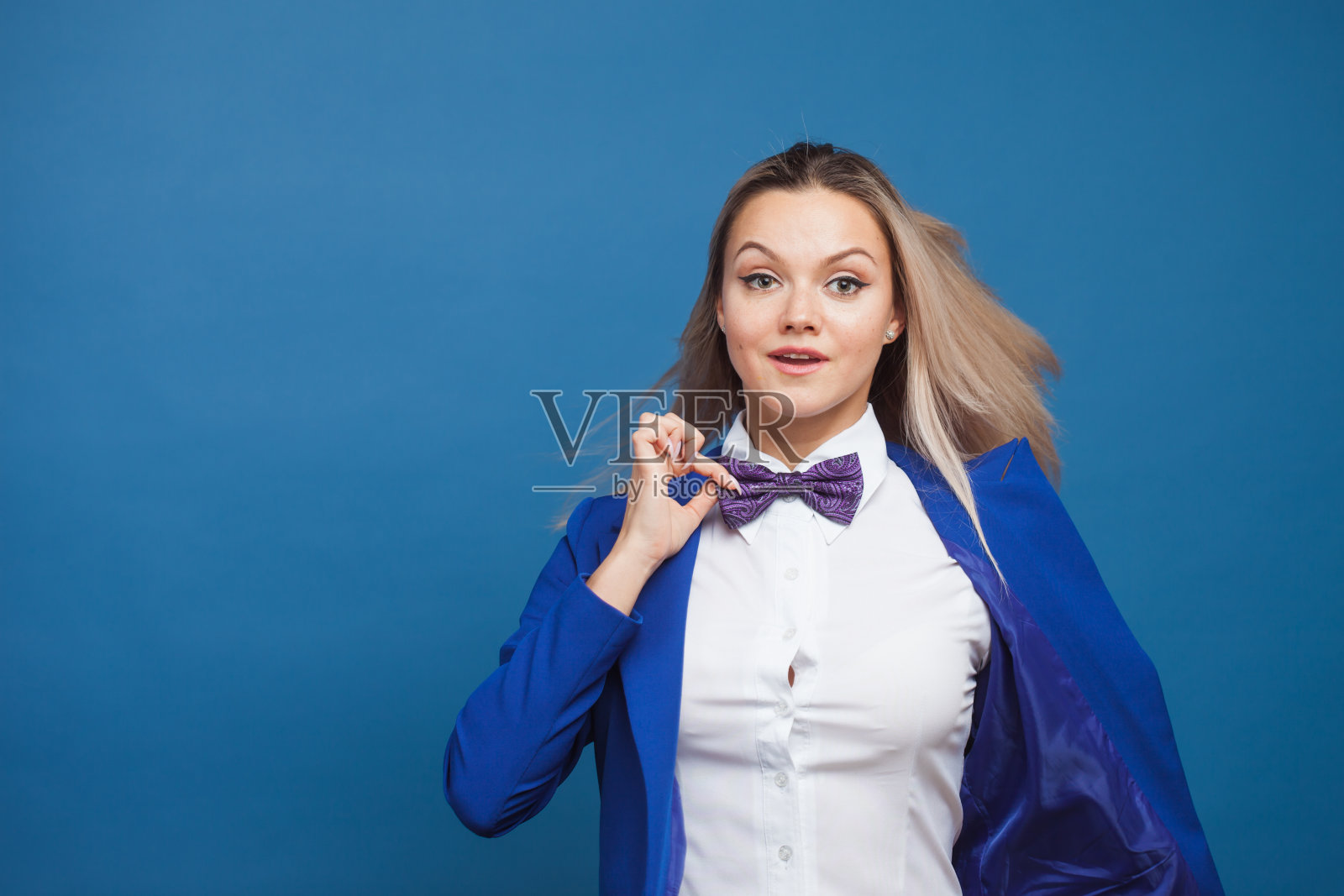 蓝色背景上穿着蓝色衣服的快乐微笑的年轻女子。友好的商业肖像照片摄影图片