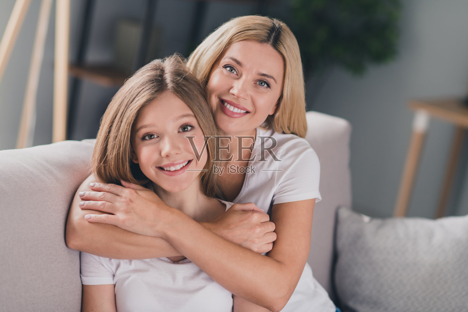漂亮可爱的女儿妈妈穿着白色t恤微笑拥抱坐在室内室内房间的沙发照片摄影图片