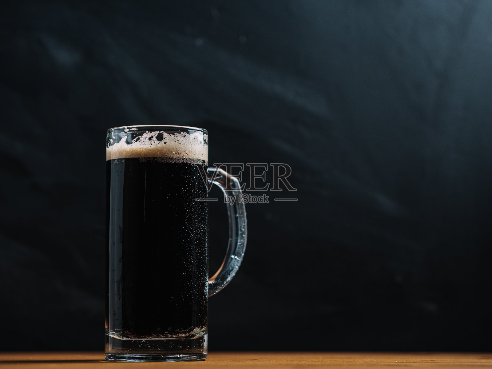 木桌上放着一大杯新鲜烈性啤酒，背景为黑色照片摄影图片