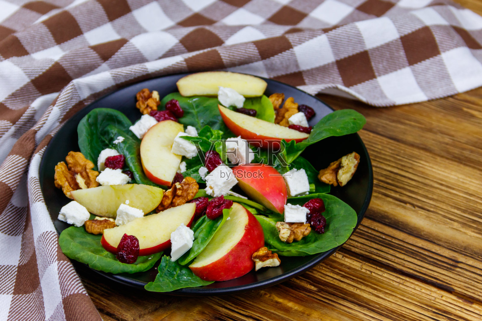 秋季菠菜沙拉配苹果，羊乳酪，核桃和蔓越莓干放在木桌上。健康的素食照片摄影图片