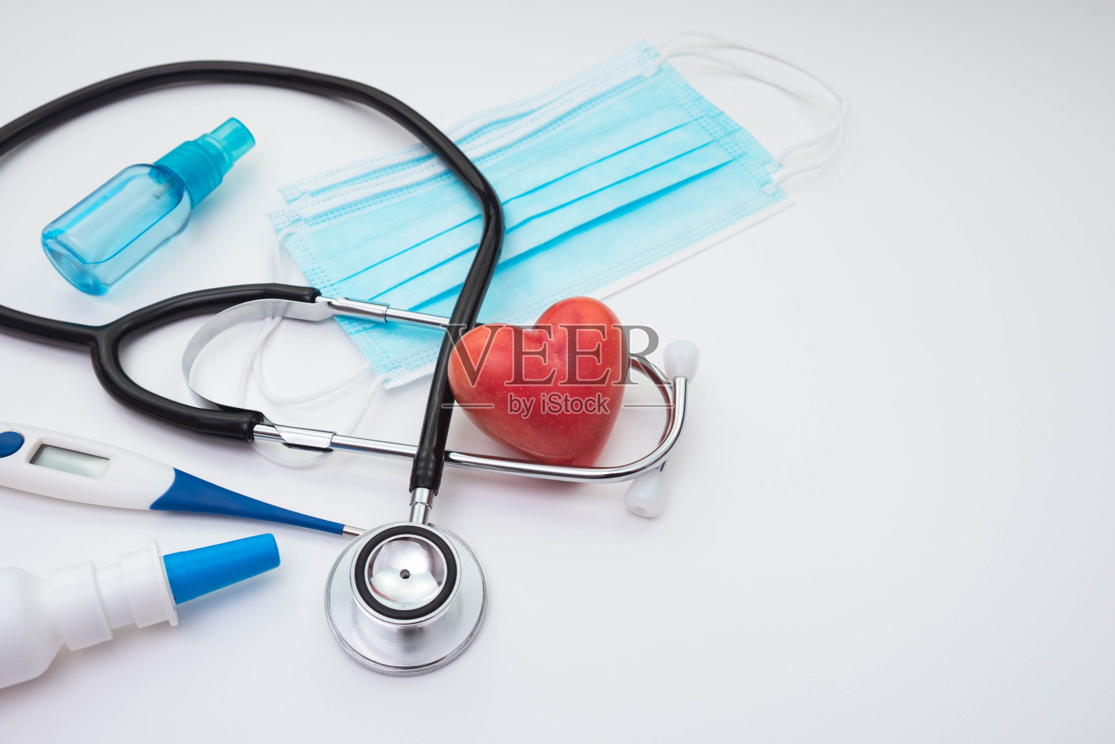 口罩、听诊器、红心、杀菌剂、体温计放在白底桌上照片摄影图片