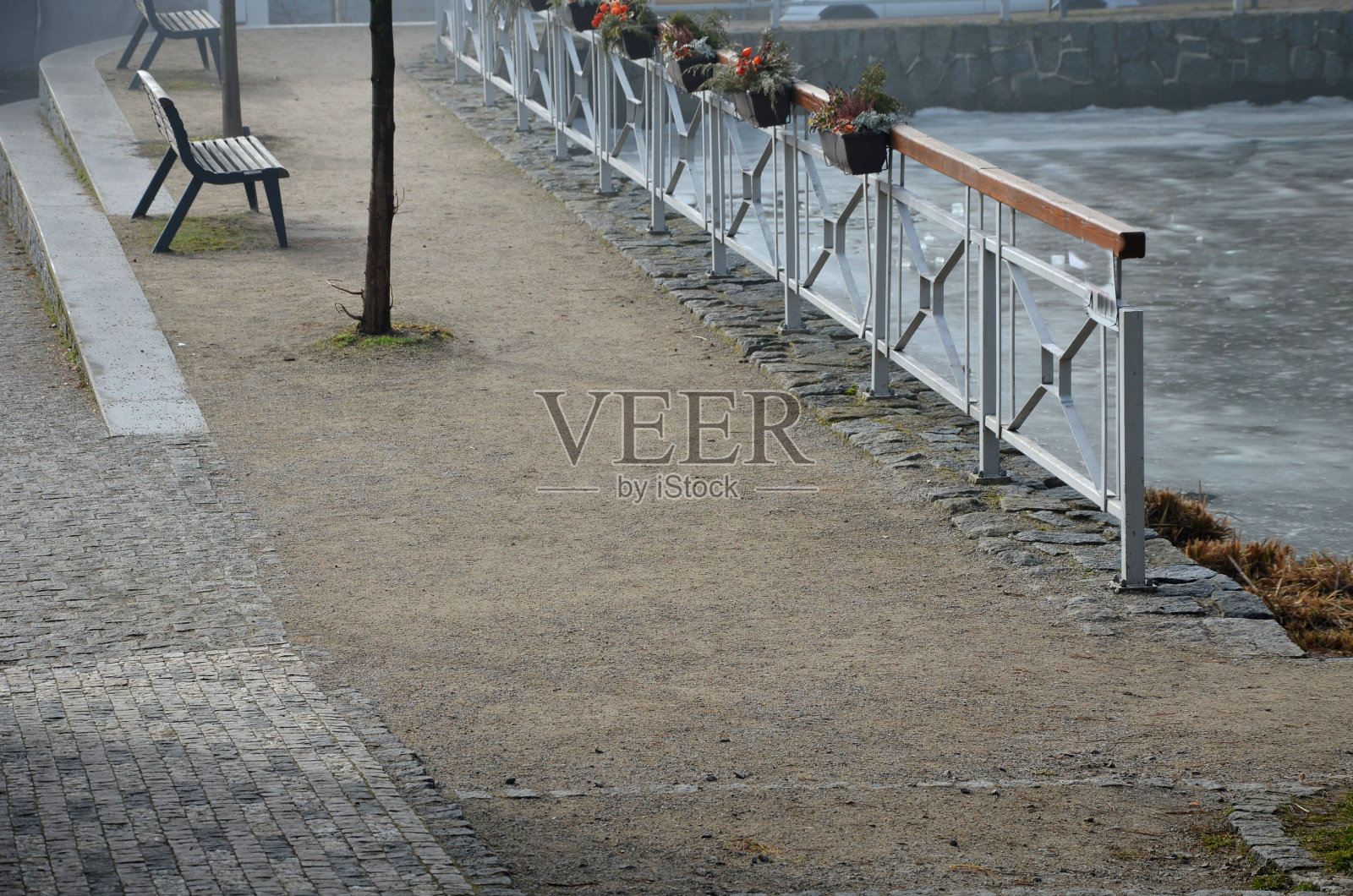 海滨，金属栏杆和塑料盒子附在扶手上。用干花装饰。池塘边有长凳和水泥楼梯。花岗岩铺面和打谷压实地面照片摄影图片