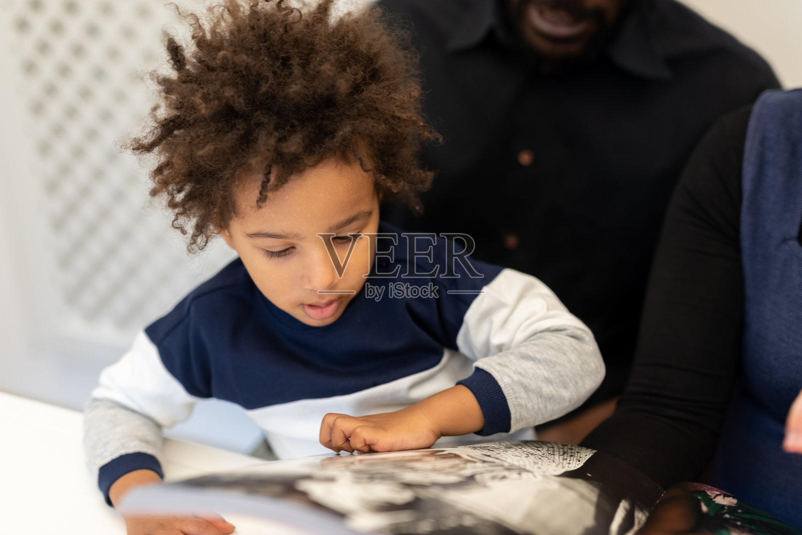 温柔的混血孩子在父亲的怀抱中为孩子们读童话故事，孩子翻阅书页时惊讶的表情的细节，父母家庭教育的概念照片摄影图片