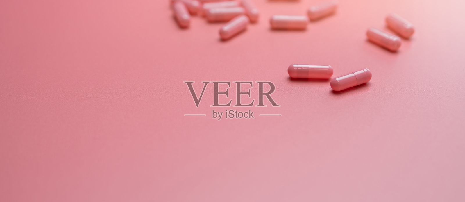 粉红色的胶囊药丸散布在粉红色的背景上。维生素和补充健康的皮肤，胶原蛋白促进，和痤疮治疗的概念。网上药店。药房商店横幅。制药行业。照片摄影图片