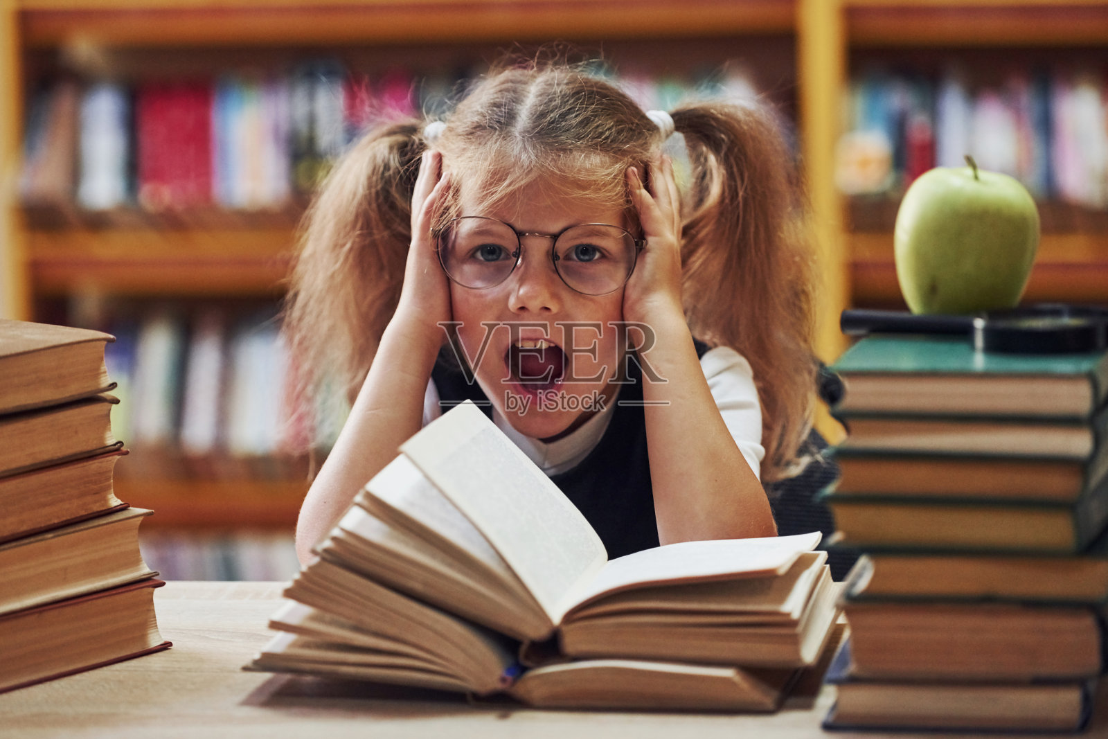 感到兴奋。梳着辫子的可爱小女孩在图书馆里。苹果上市照片摄影图片