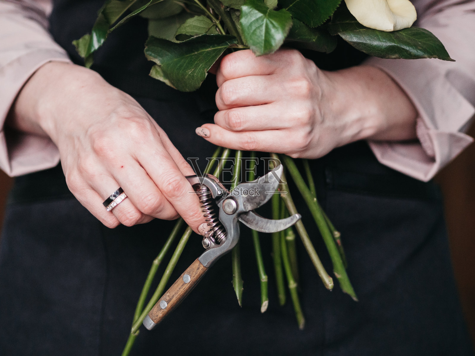 一个花商正在创作一幅作品，一个花童手里拿着修枝器，正在收集一束玫瑰。照片摄影图片