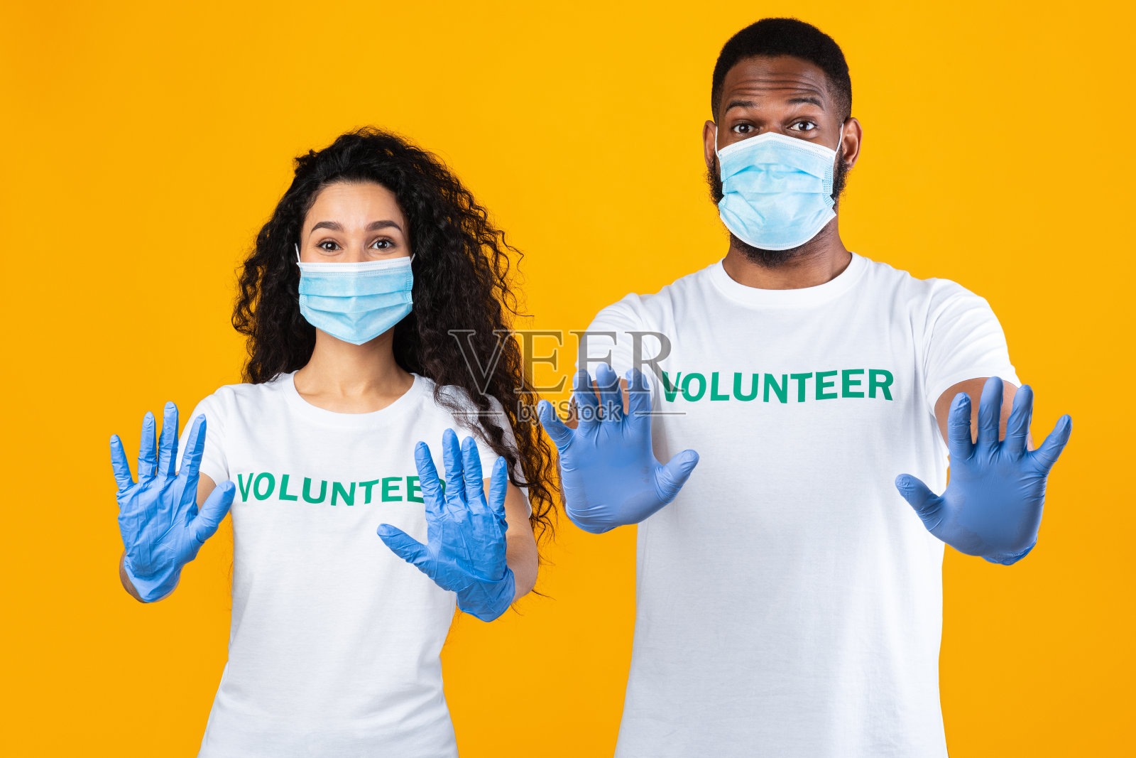 两名志愿者在黄色背景下示意停止戴口罩照片摄影图片