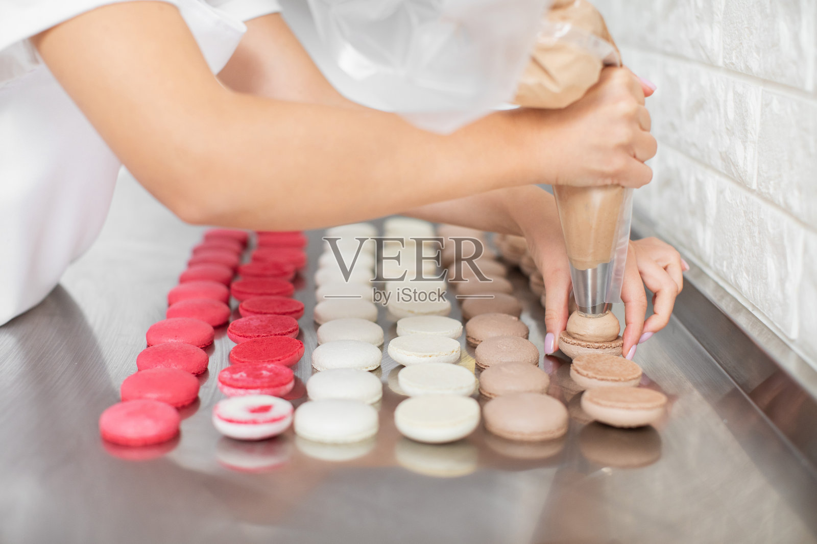 马卡龙的制造，一步一步的流程。近距离图片的女性巧克力甘纳许坐在巧克力马卡龙壳上。照片摄影图片