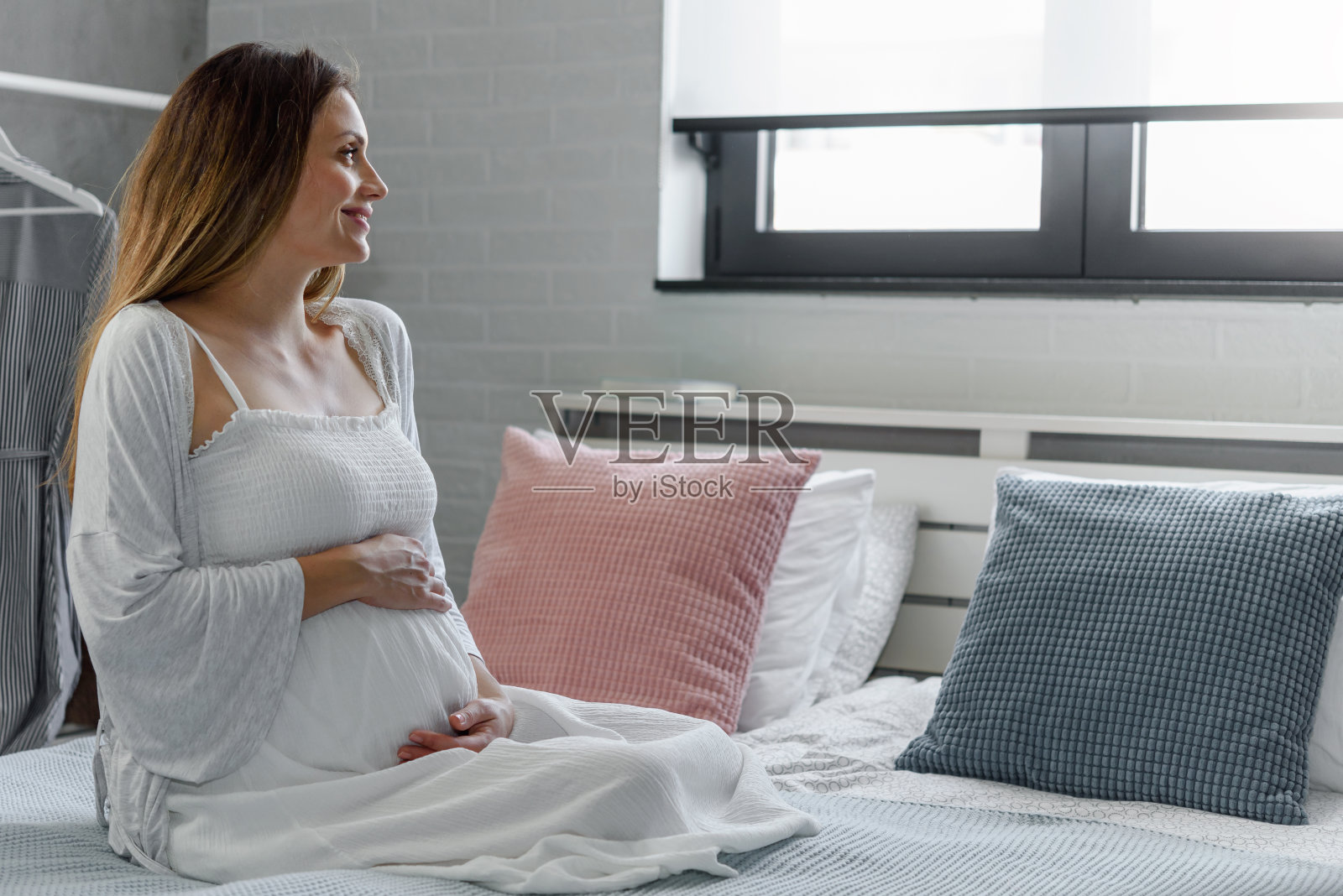 一个美丽的孕妇在家里的床上抱着她的肚子照片摄影图片