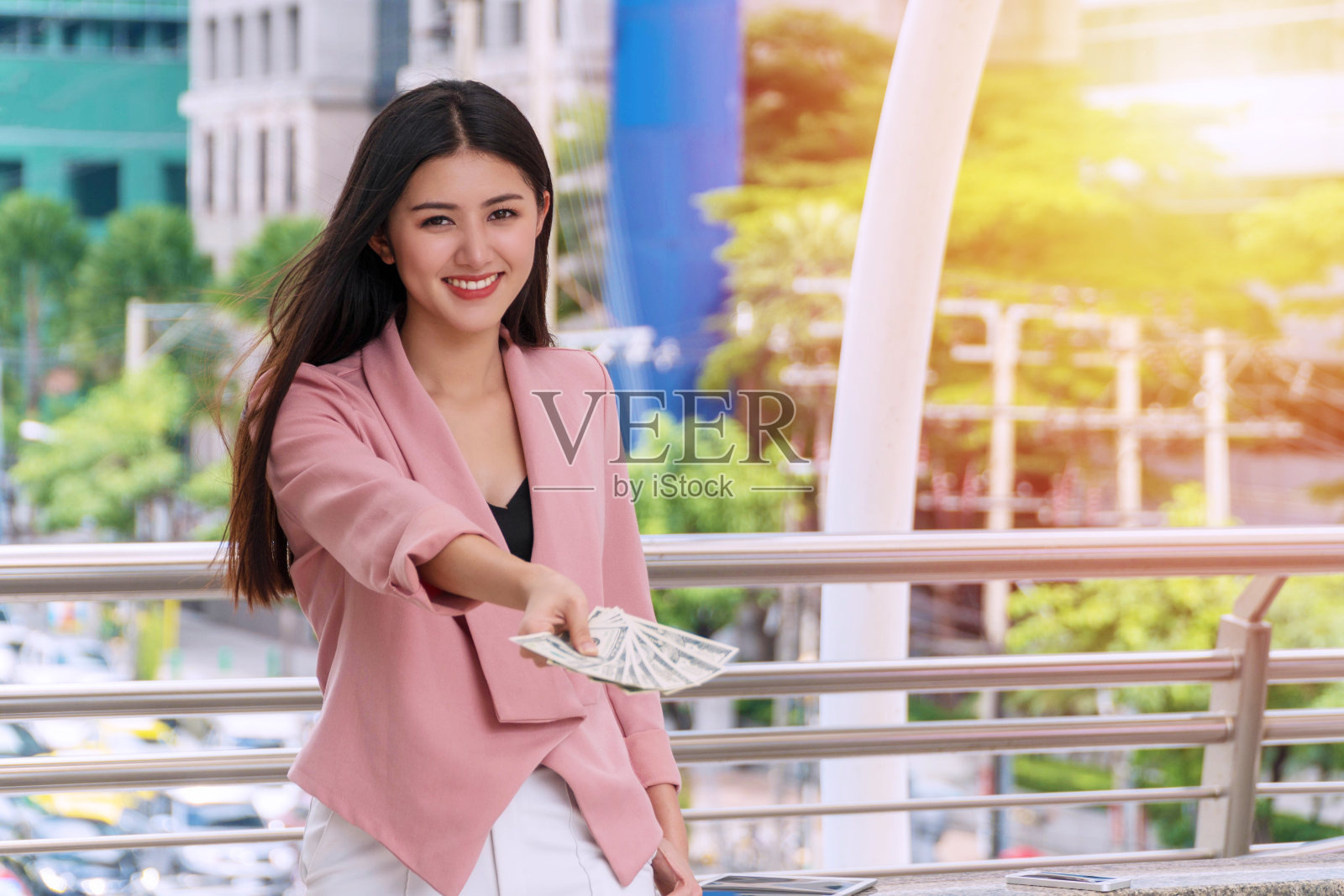 迷人的年轻女商人拿着美元现金在她的手，而站在城市的背景。商业和金钱的概念。照片摄影图片