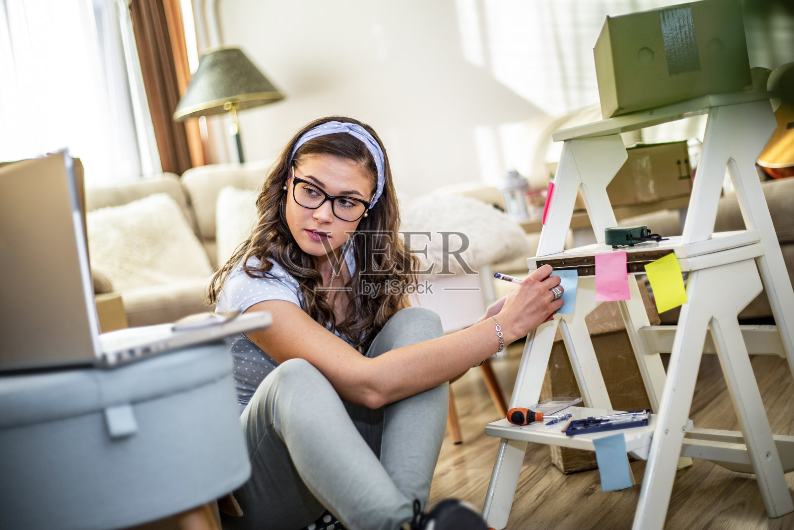 一个年轻女人要搬去新公寓了。一个年轻漂亮的女人坐在新房子的地板上。一个快乐的女人在她的新家把东西从箱子里拿出来的肖像。照片摄影图片