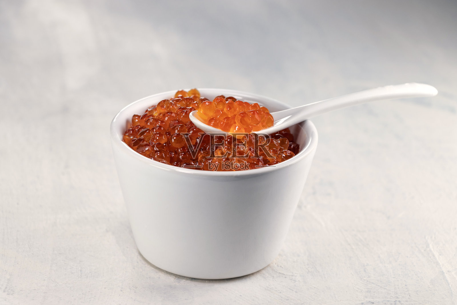 美味的，易碎的，大的红色鱼子酱放在白色的杯子里，勺子放在白色的背景上照片摄影图片