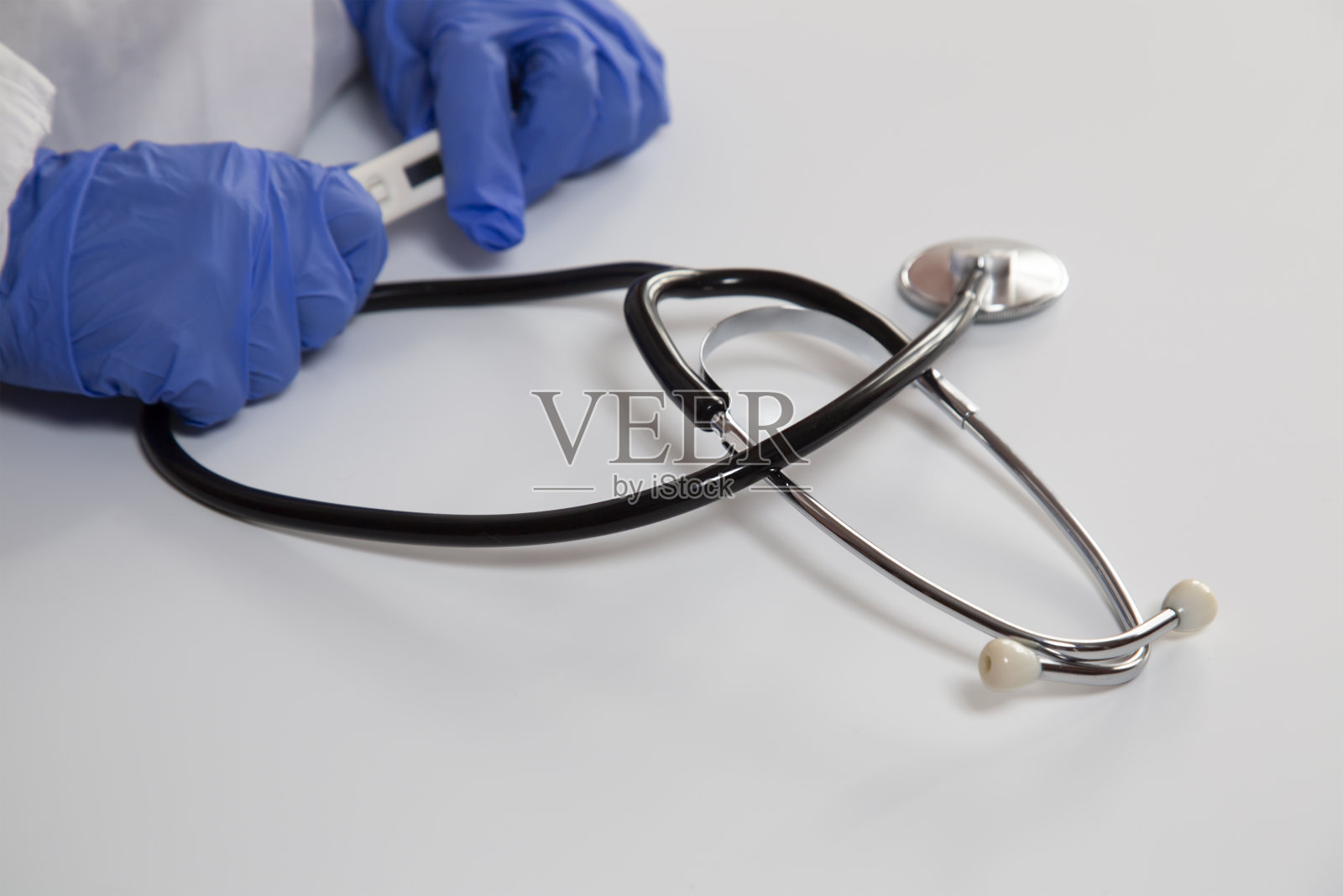 医生戴着蓝手套的手拿着一个电子温度计。照片摄影图片