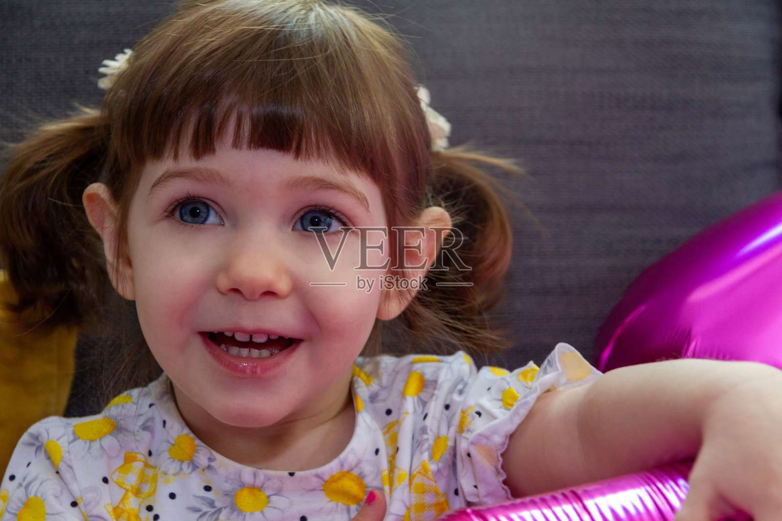 小女孩坐在沙发上，手里拿着粉色的气球照片摄影图片