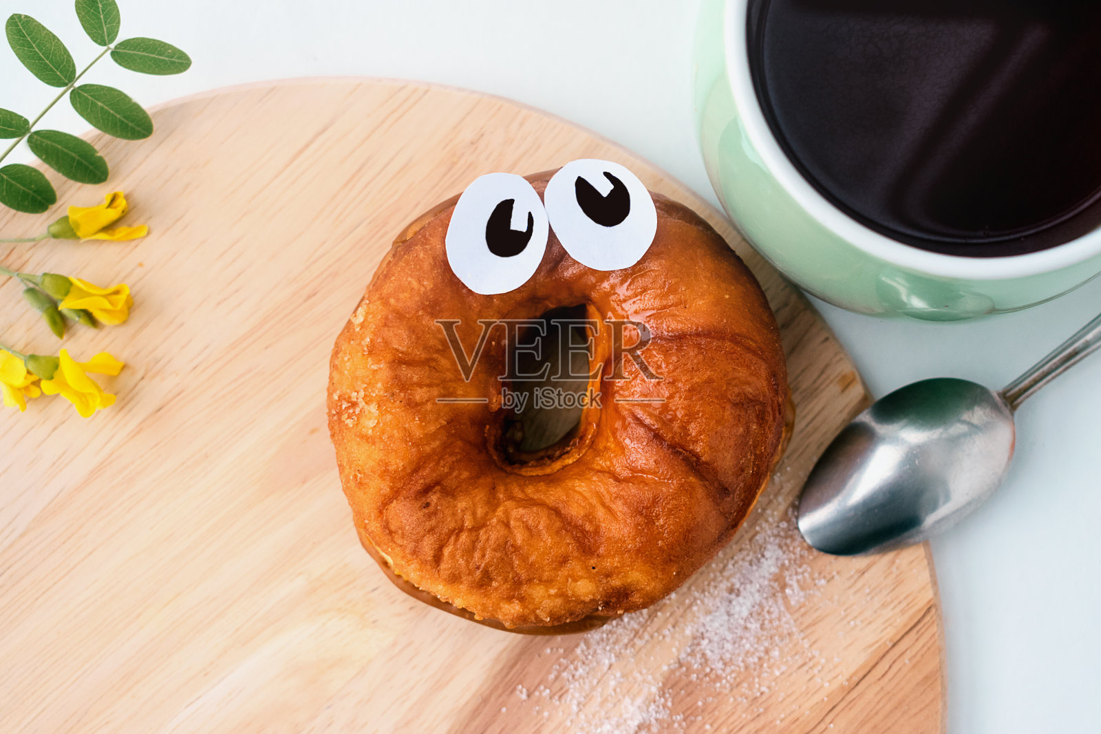 一个带着纸眼睛的吓坏了的甜甜圈躺在一块木头砧板上，旁边放着一杯茶。极具创意的食物概念。国家甜甜圈日照片摄影图片