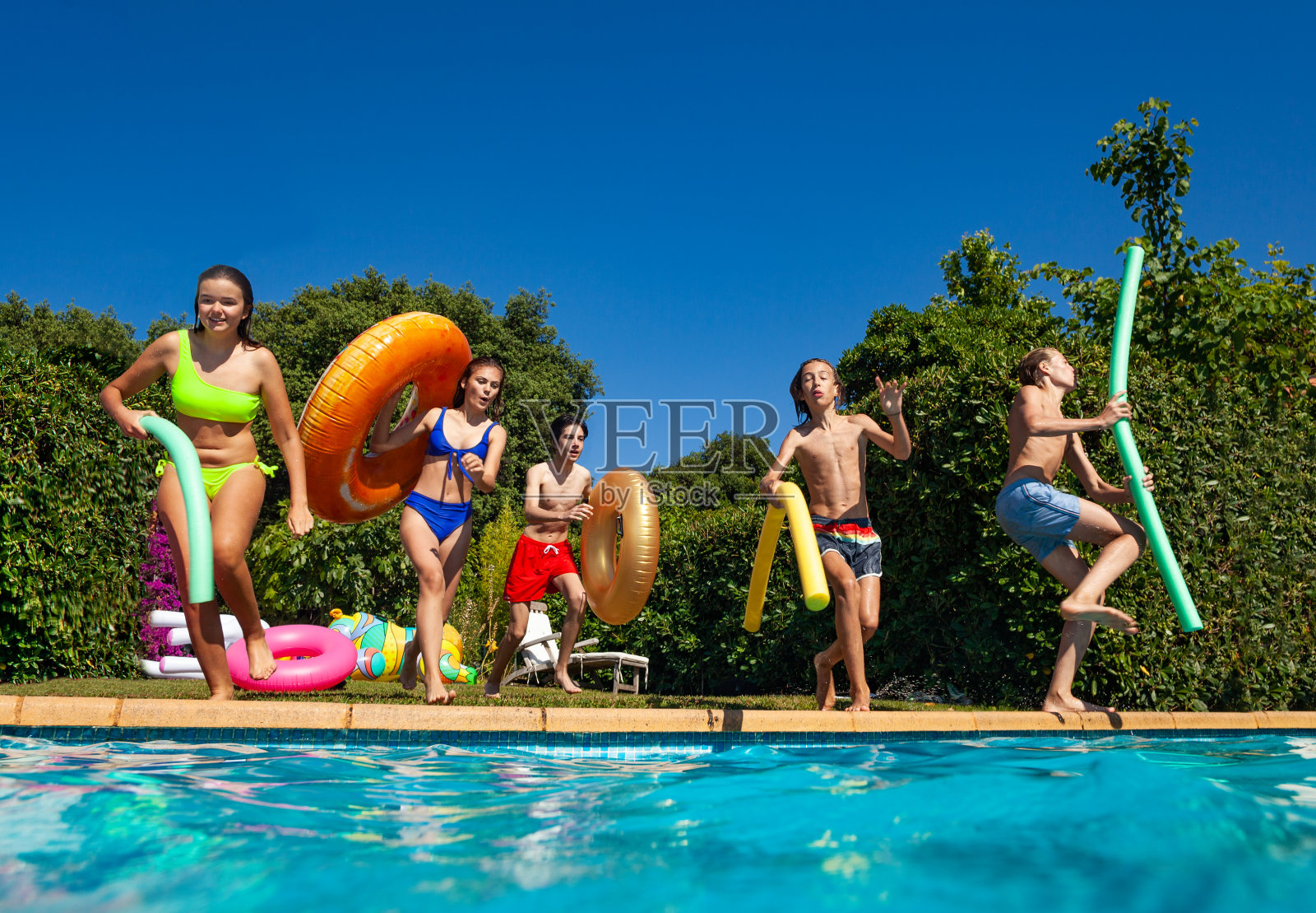 一群孩子带着游泳池玩具在水里跳水照片摄影图片