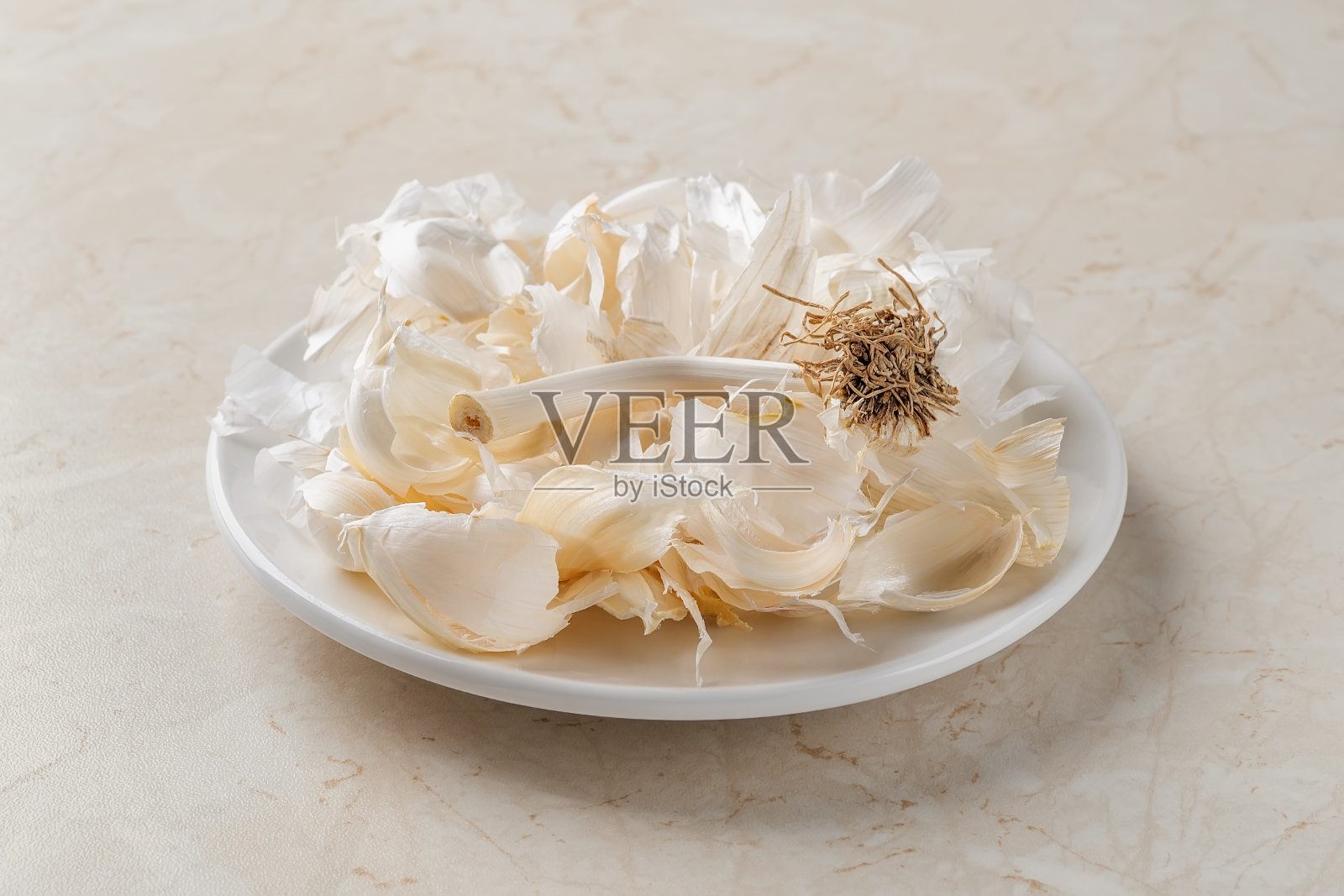 将白蒜皮放在厨房桌子上方的小盘子上。在家做饭和装罐头。可生物降解的食物垃圾和果皮。特写镜头。照片摄影图片