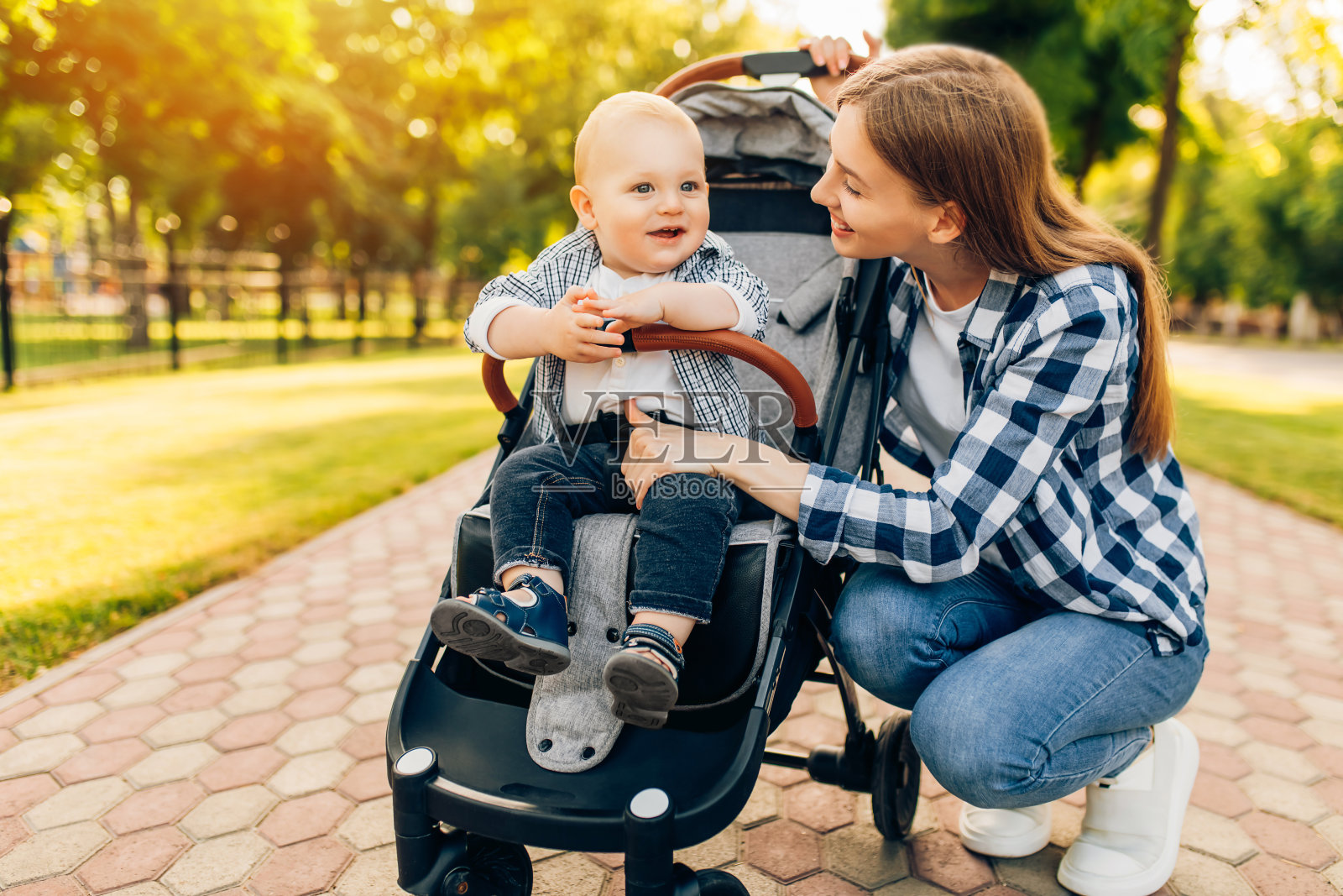 在一个阳光明媚的夏日，妈妈带着她可爱的孩子在公园里散步。照片摄影图片