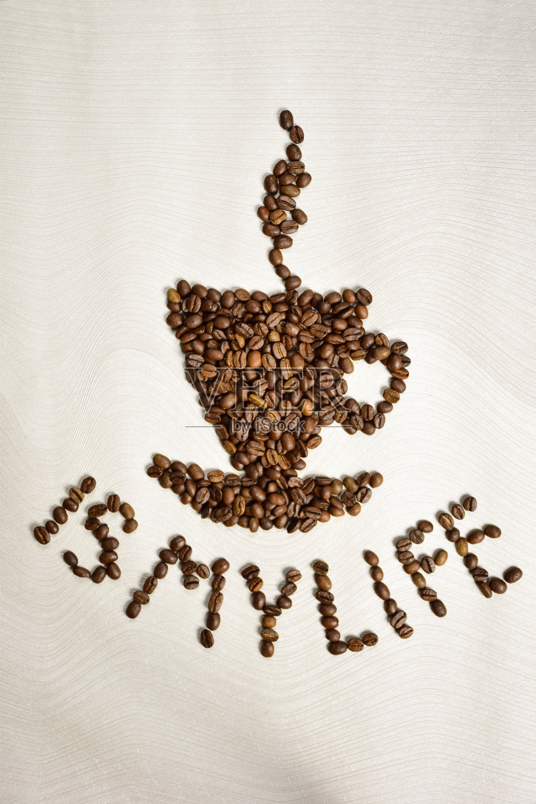 用咖啡豆摆出一个咖啡杯和茶托的形状，在它下面刻着“咖啡是我的生命”照片摄影图片