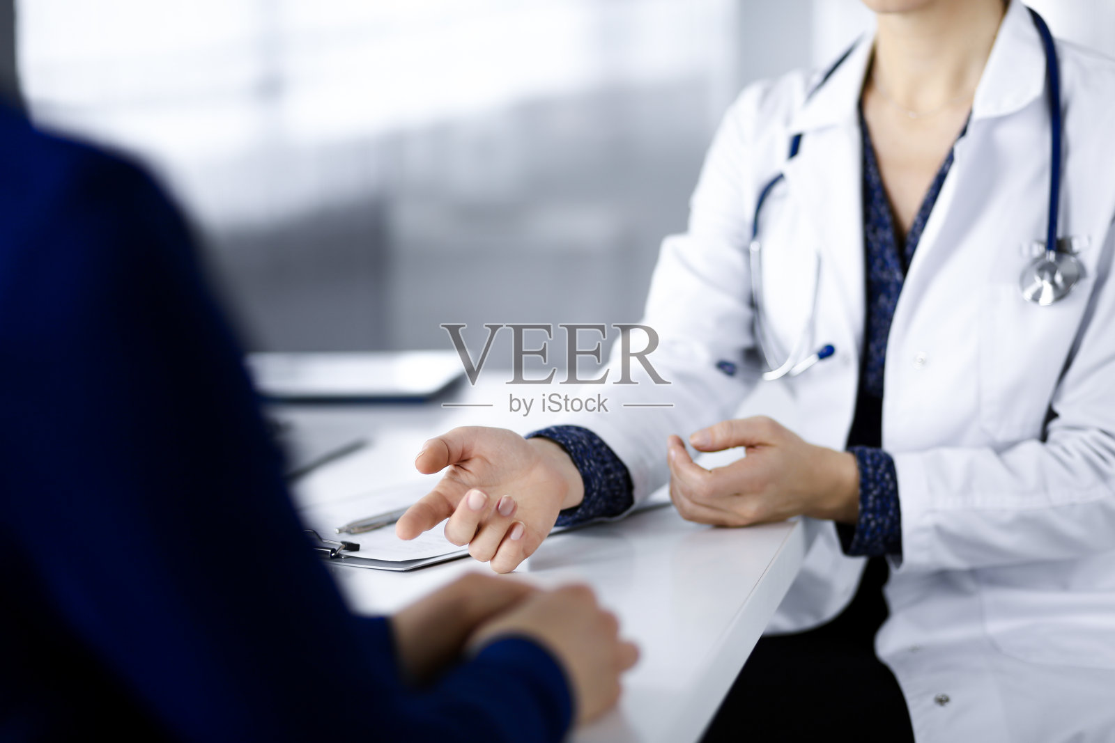 一个不知名的女医生正在和她的病人谈论她的诊断，而坐在一起在一个诊所的橱柜的桌子上。医生在工作的地方，特写。医院里完美的医疗服务。医学的概念照片摄影图片