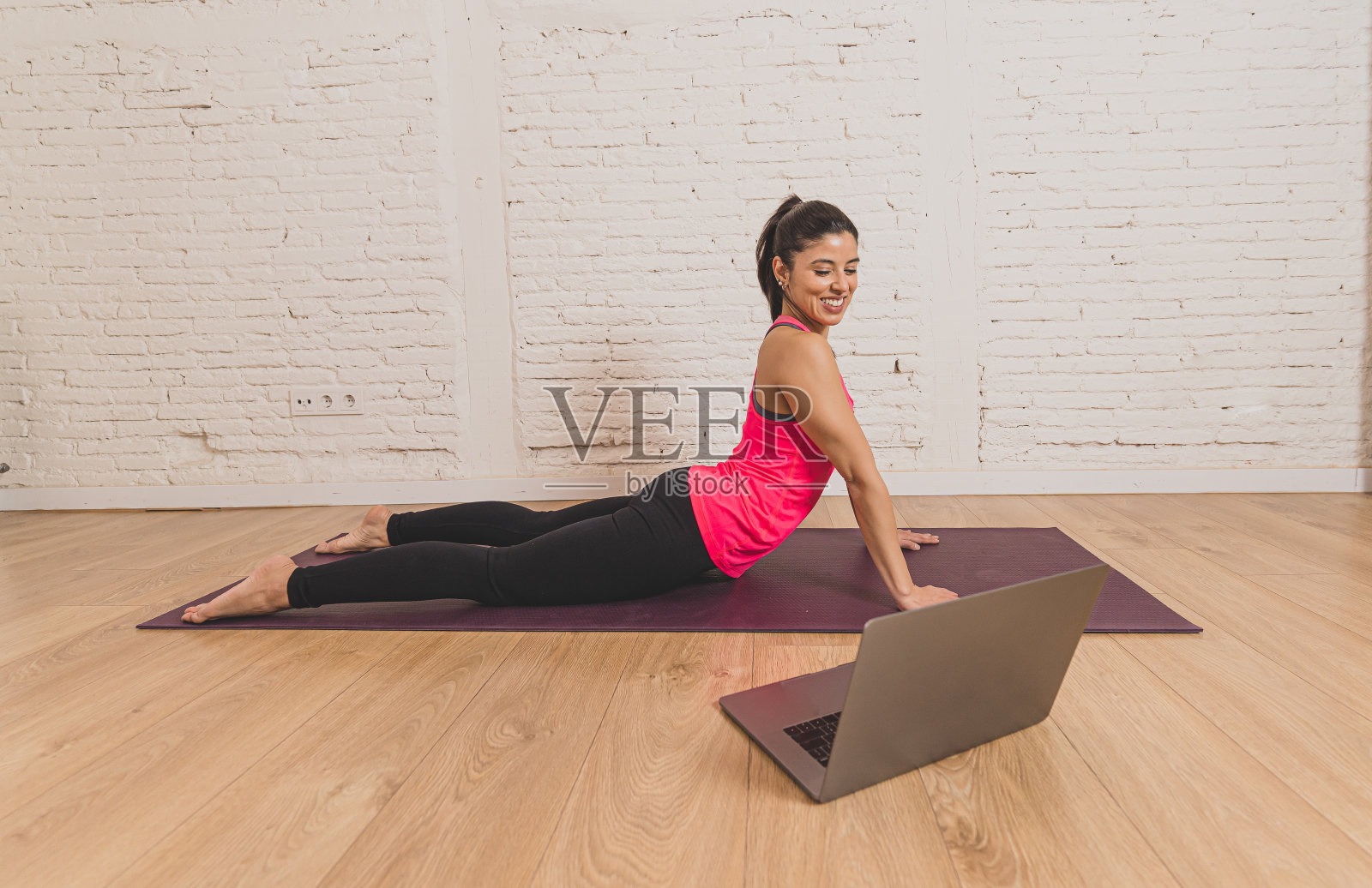 年轻漂亮的拉丁女人在家里锻炼连接到在线健身课程的电脑笔记本电脑。女私人教练教练在直播健身课上zoom教学练习。照片摄影图片