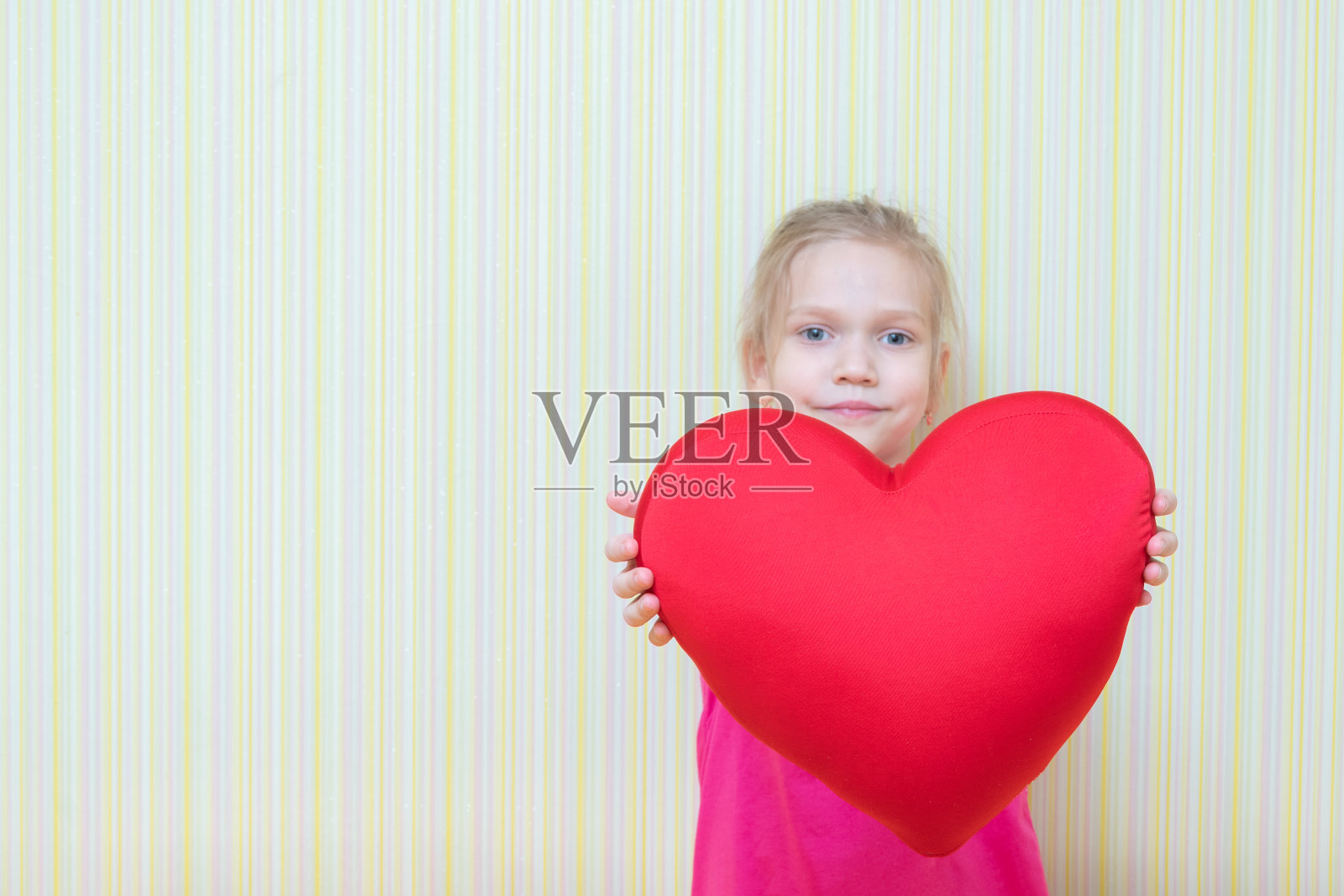 可爱的小女孩给你看了一个心形枕头，复制空间。生日快乐礼物，情人节快乐概念照片摄影图片