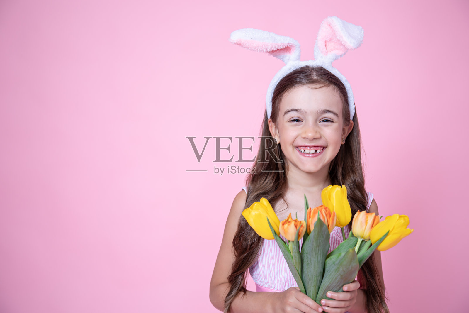 有趣的小女孩用复活节兔子耳朵拿着一束春天的花拷贝空间。照片摄影图片