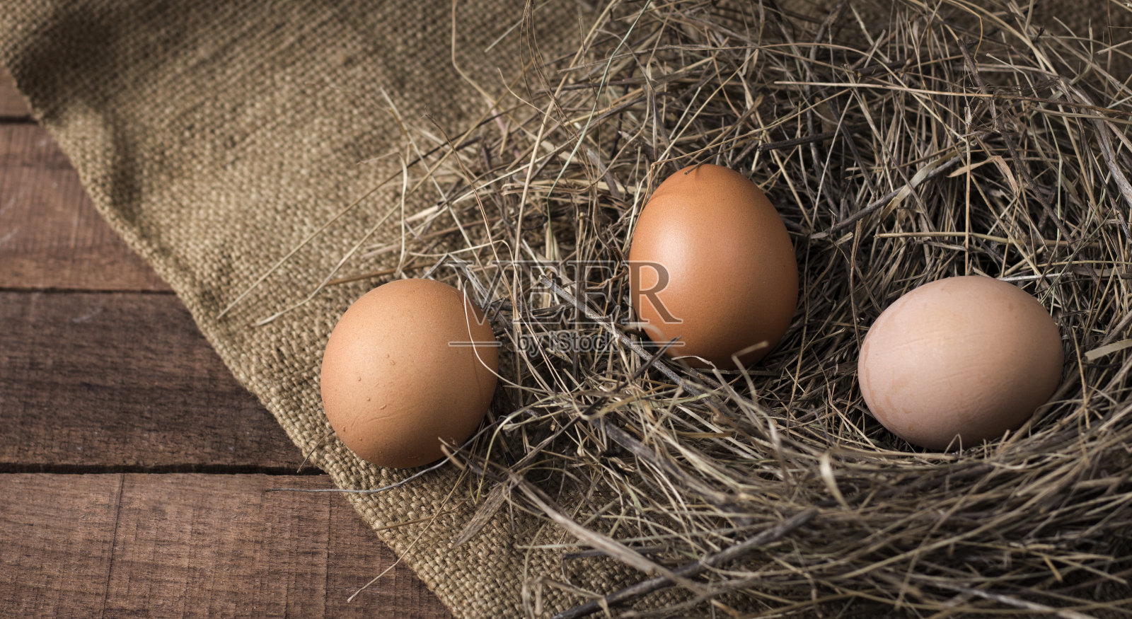 三个鸡蛋在一窝干草上，在一个木头表面的粗麻布背景，俯视图照片摄影图片