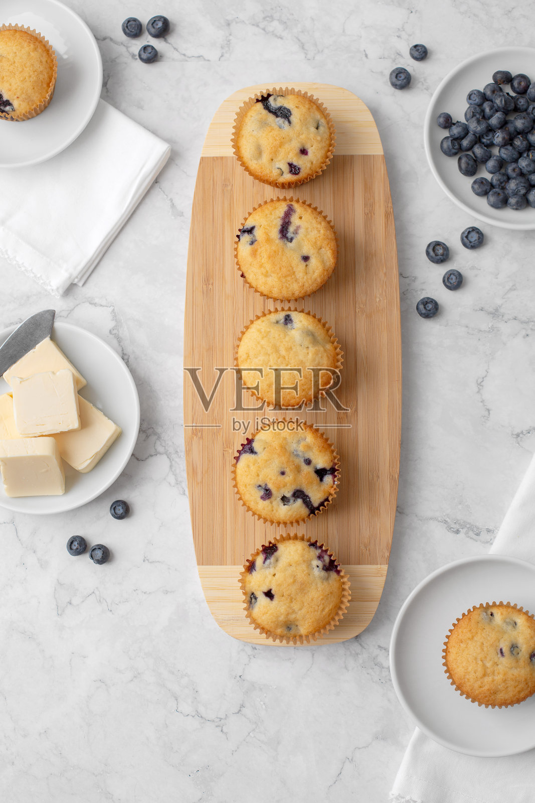 俯视图蓝莓松饼在木板上;背景蓝莓和黄油;两个松饼放在白盘子里照片摄影图片