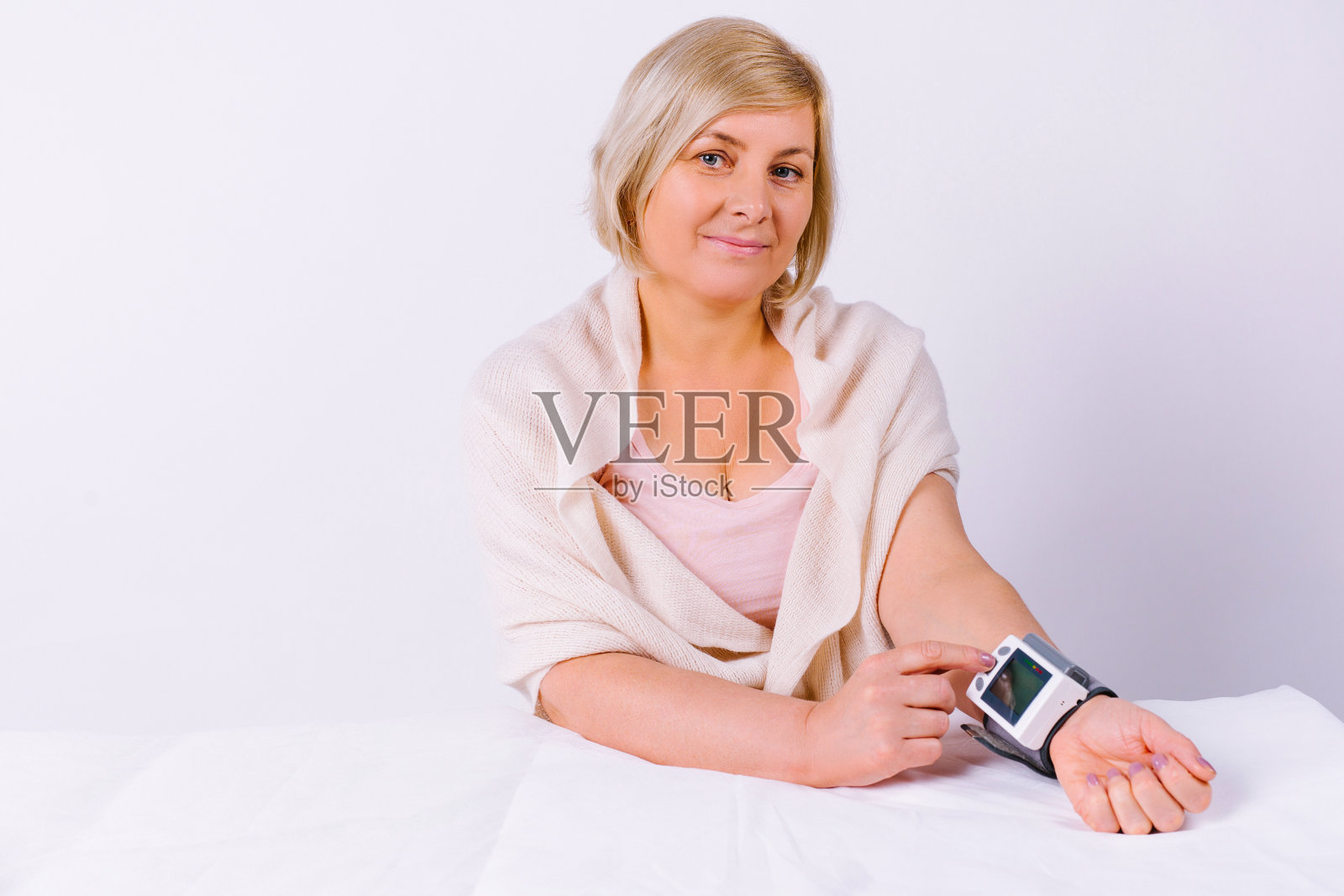 一个可爱的资深金发女人看着相机，在数字设备上测量血压。白色背景和空白的边空间。照片摄影图片