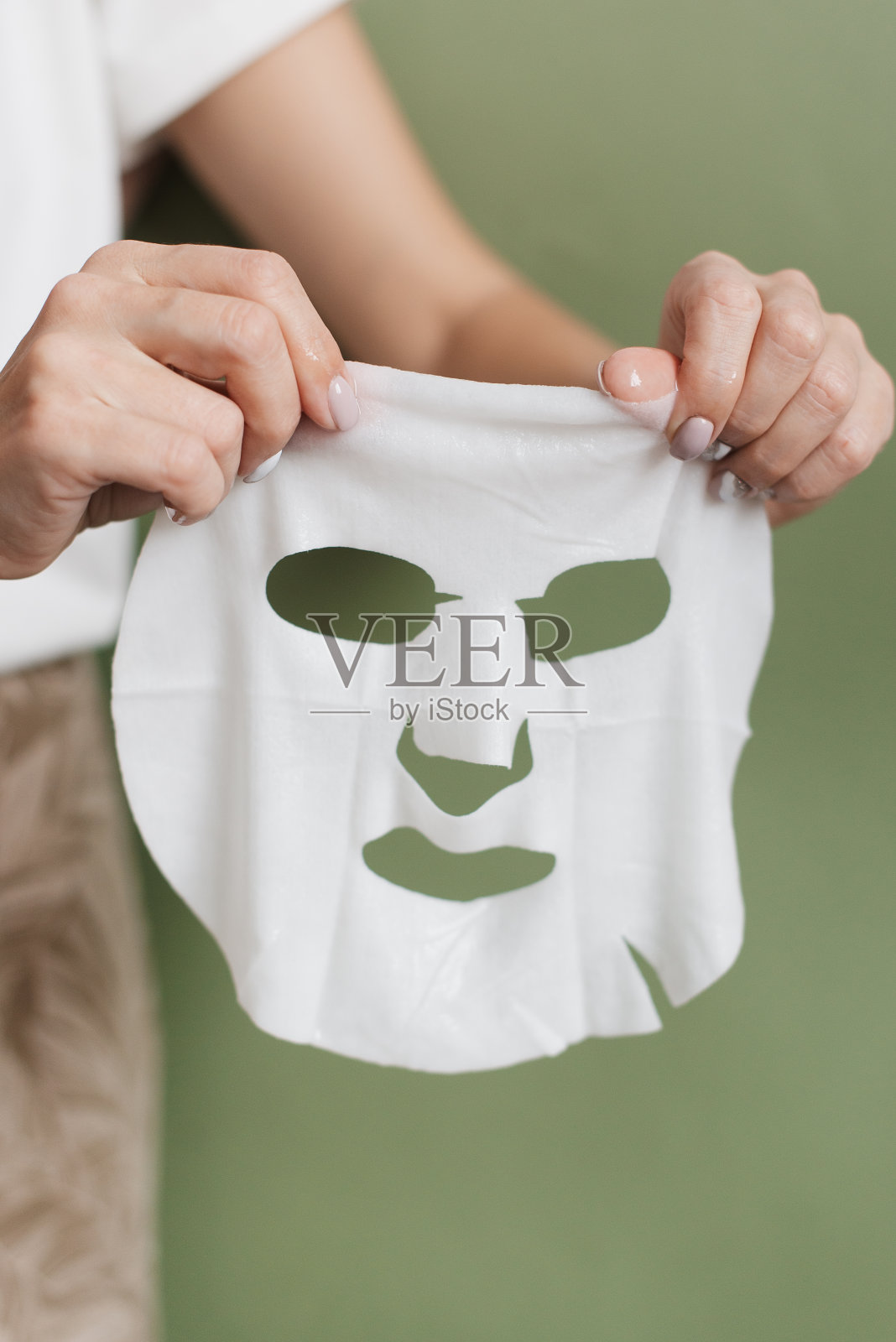 一个女人的手上拿着一个白色的布面罩。化妆面膜上的绿色背景。照片摄影图片