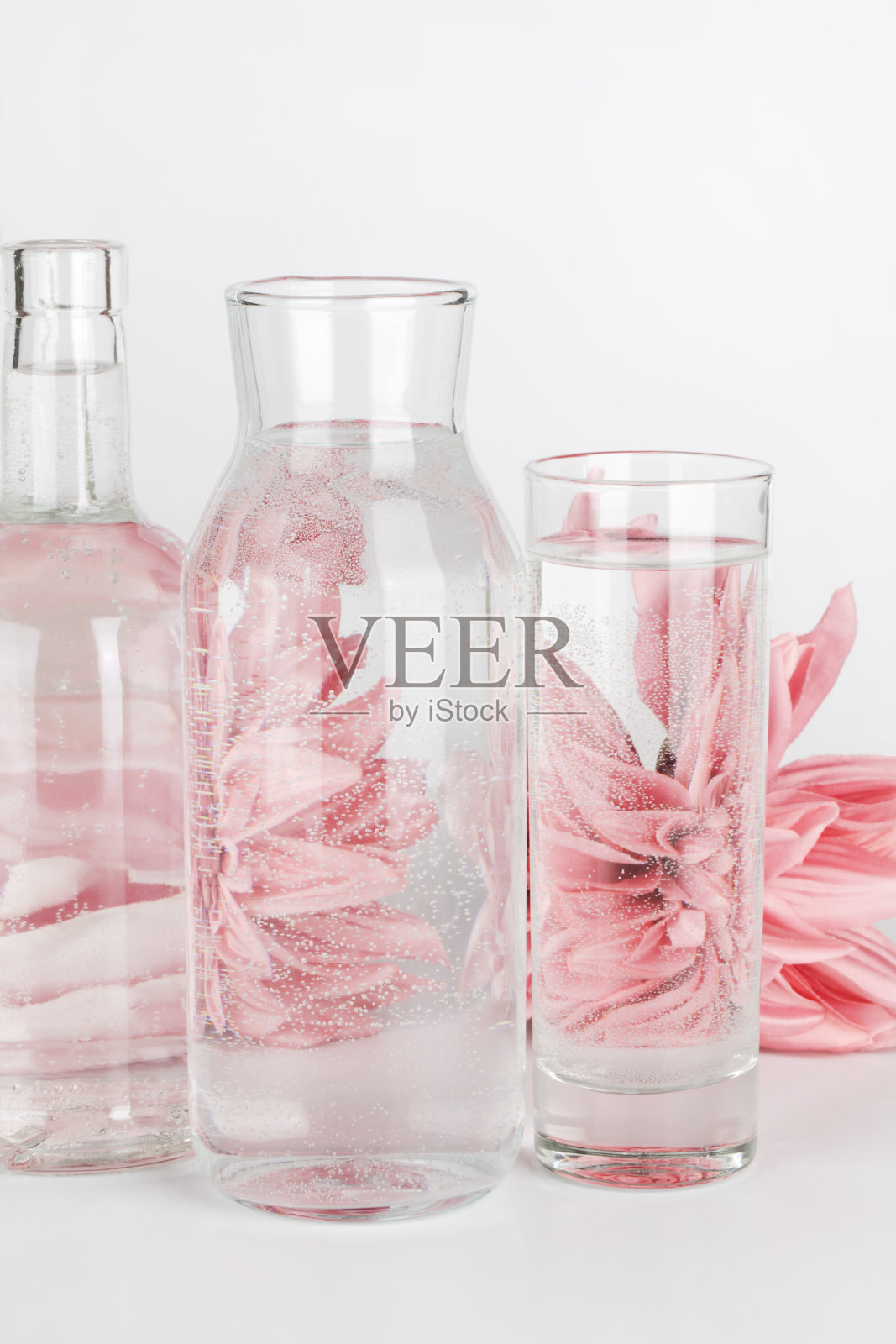 粉红色的花朵在白色背景的玻璃杯和瓶子中的水中扭曲。家居装饰，环保，放松，园艺的概念。照片摄影图片