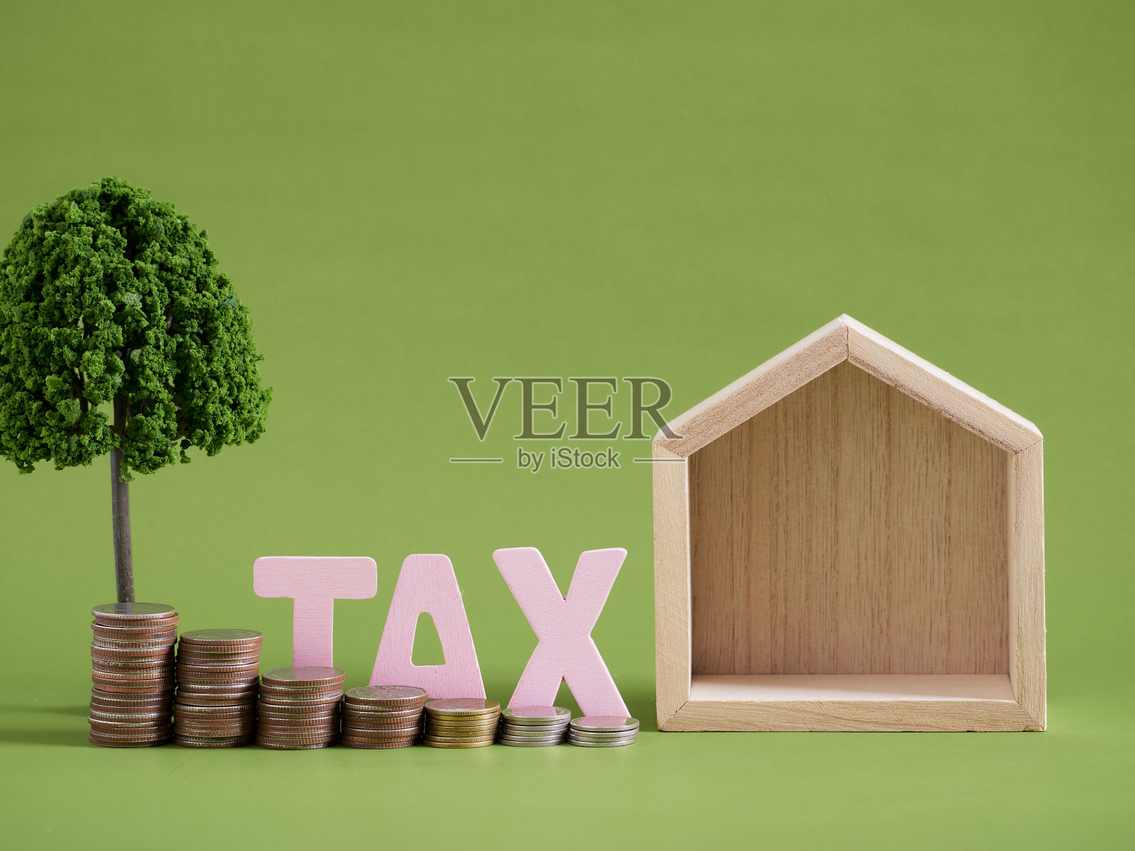 纳税时间。绿色背景上的木制房屋模型和硬币照片摄影图片