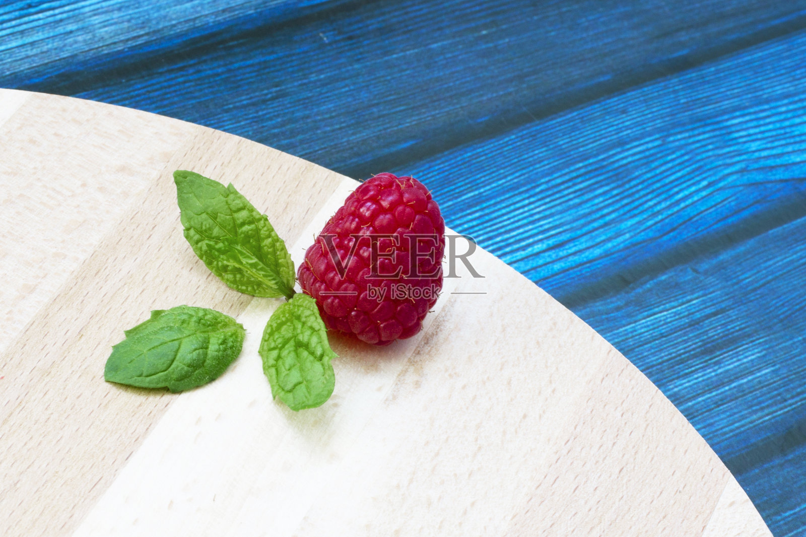 木桌上放着新鲜的覆盆子和薄荷。成熟的红覆盆子和绿色的薄荷叶放在木架子上照片摄影图片