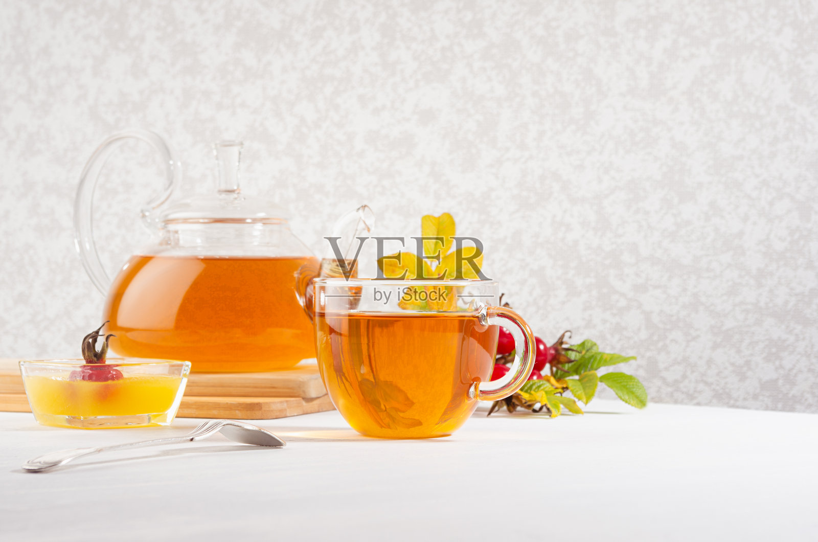 玫瑰果茶与茶壶，杯，蜂蜜，秋天玫瑰果枝在阳光明媚的日子里在白色的木桌复制空间。照片摄影图片
