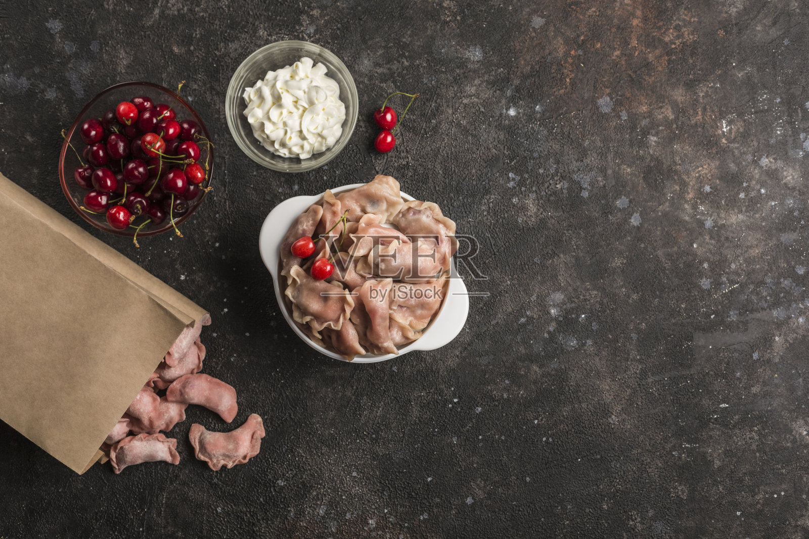 红色饺子，碗里有樱桃，环保的纸包装，黑色的背景是白色的酱汁。照片摄影图片