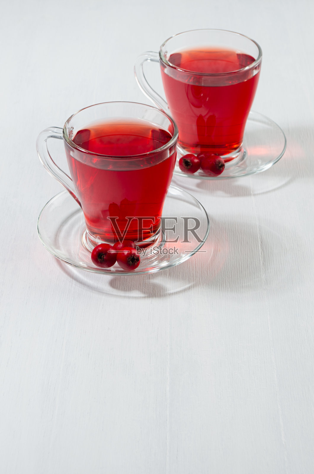 健康的红色草药茶在透明的杯子与成熟的山楂浆果在阳光下在白色木板，复制空间，垂直。照片摄影图片