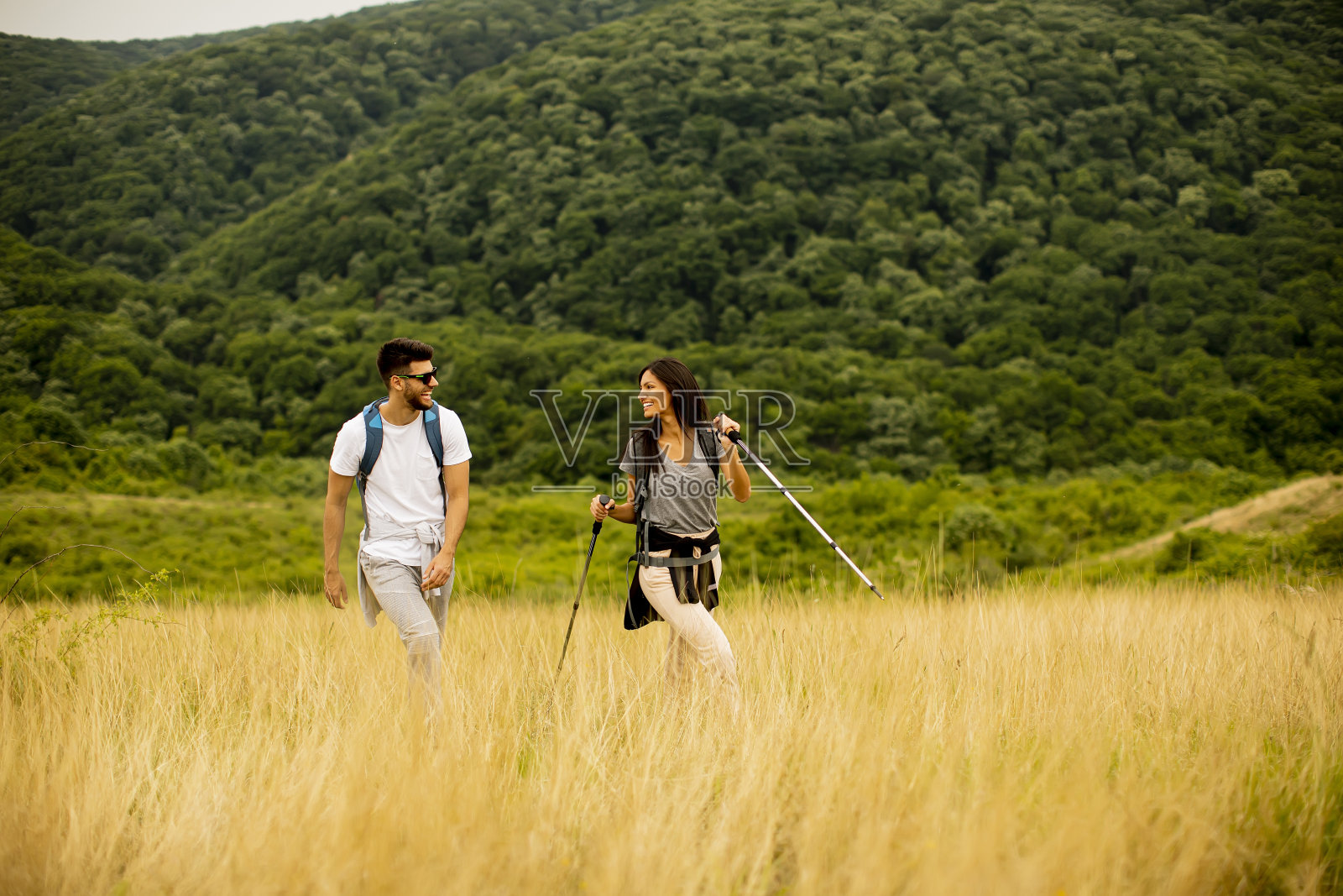 微笑的夫妇背着背包走过绿色的山丘照片摄影图片