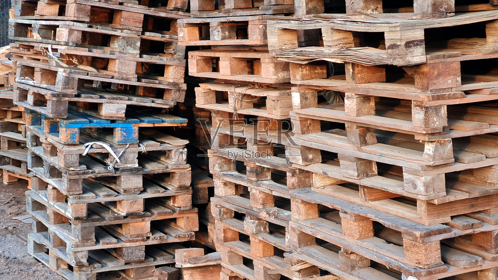 在货物配送企业的仓库中，有大量的废旧木托盘堆放在户外。照片摄影图片