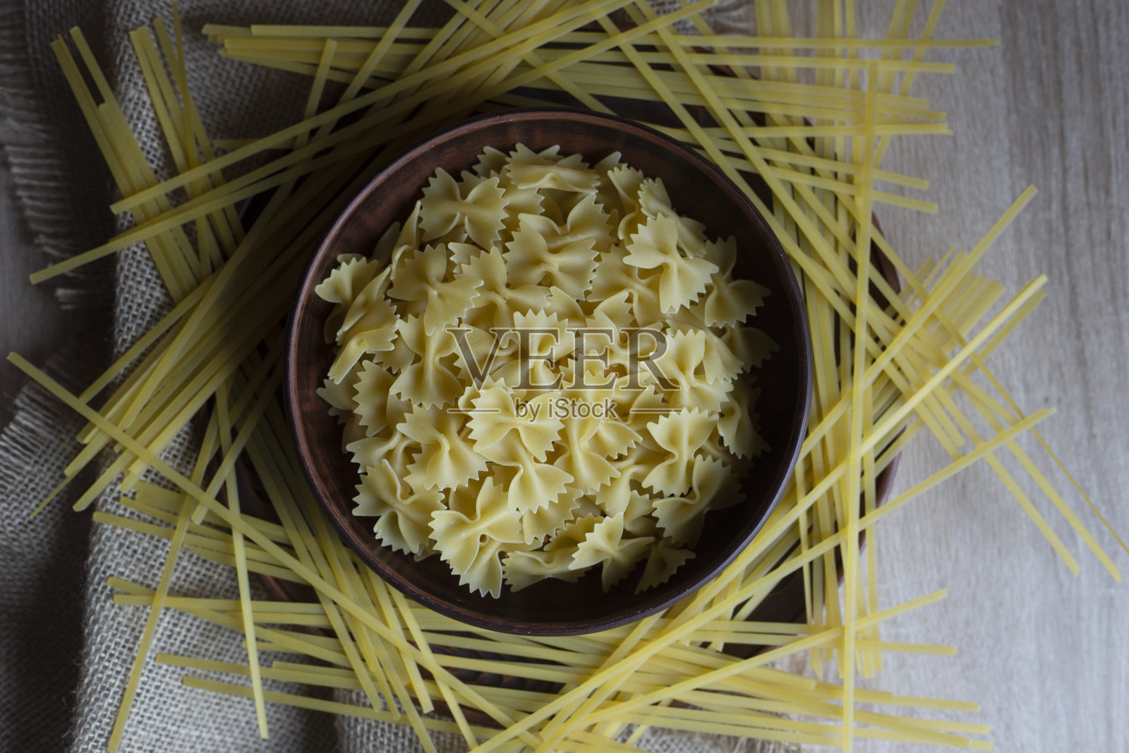 各种各样的意大利面放在棕色的老式盘子里，放在一张木桌上，用粗麻布包裹，俯视图照片摄影图片