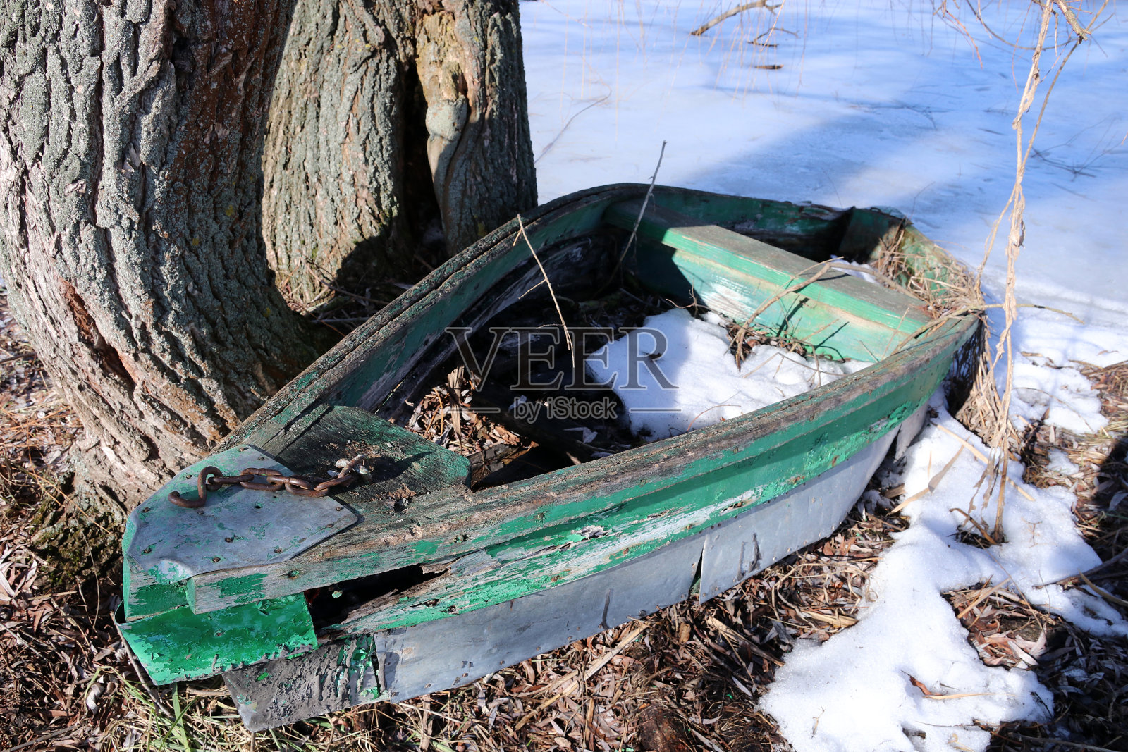 结冰的湖边有一条废弃的旧木船。照片摄影图片