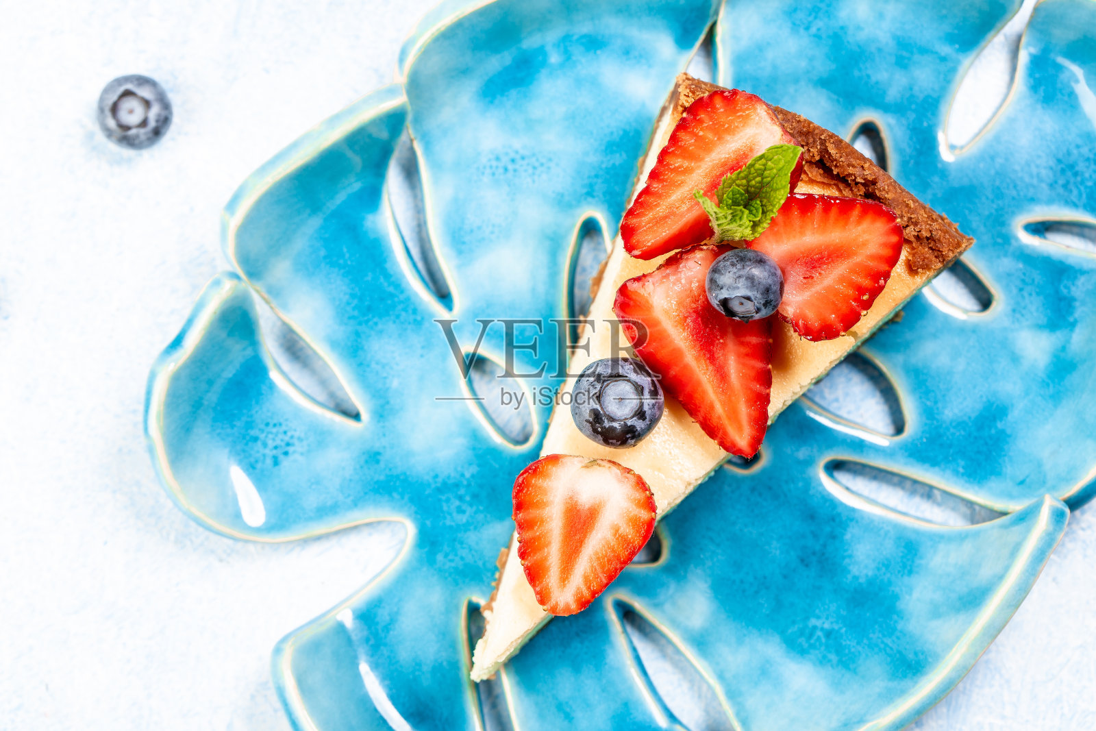 在一个蓝色的盘子上，用薄荷叶装饰的草莓和蓝莓芝士蛋糕照片摄影图片