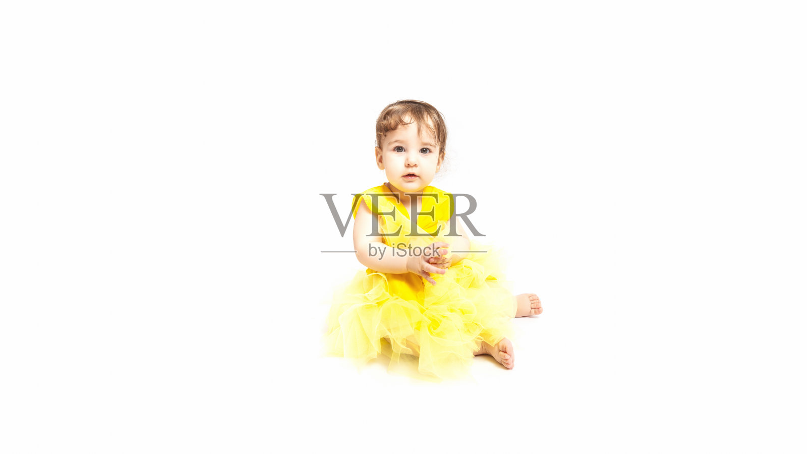 肖像可爱的白人9个月大的婴儿在黄色的裙子坐在白色的背景照片摄影图片