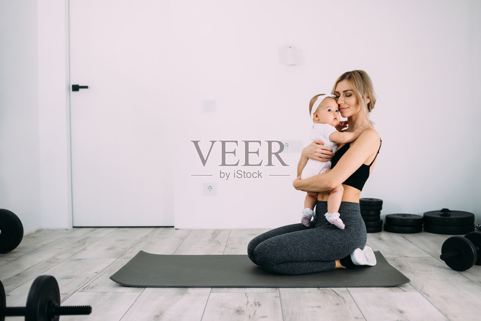 年轻美丽的母亲抱着女儿在做完瑜伽后坐在房间的地板上。在家做运动。照片摄影图片