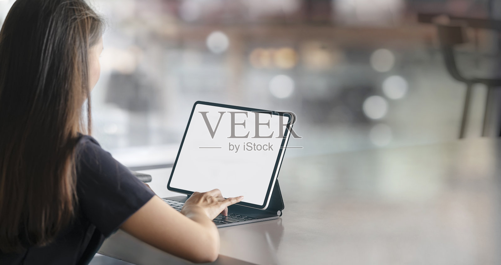 后视图的年轻女子工作在平板电脑与魔法键盘，而坐在桌子上，空白屏幕的图形设计。照片摄影图片