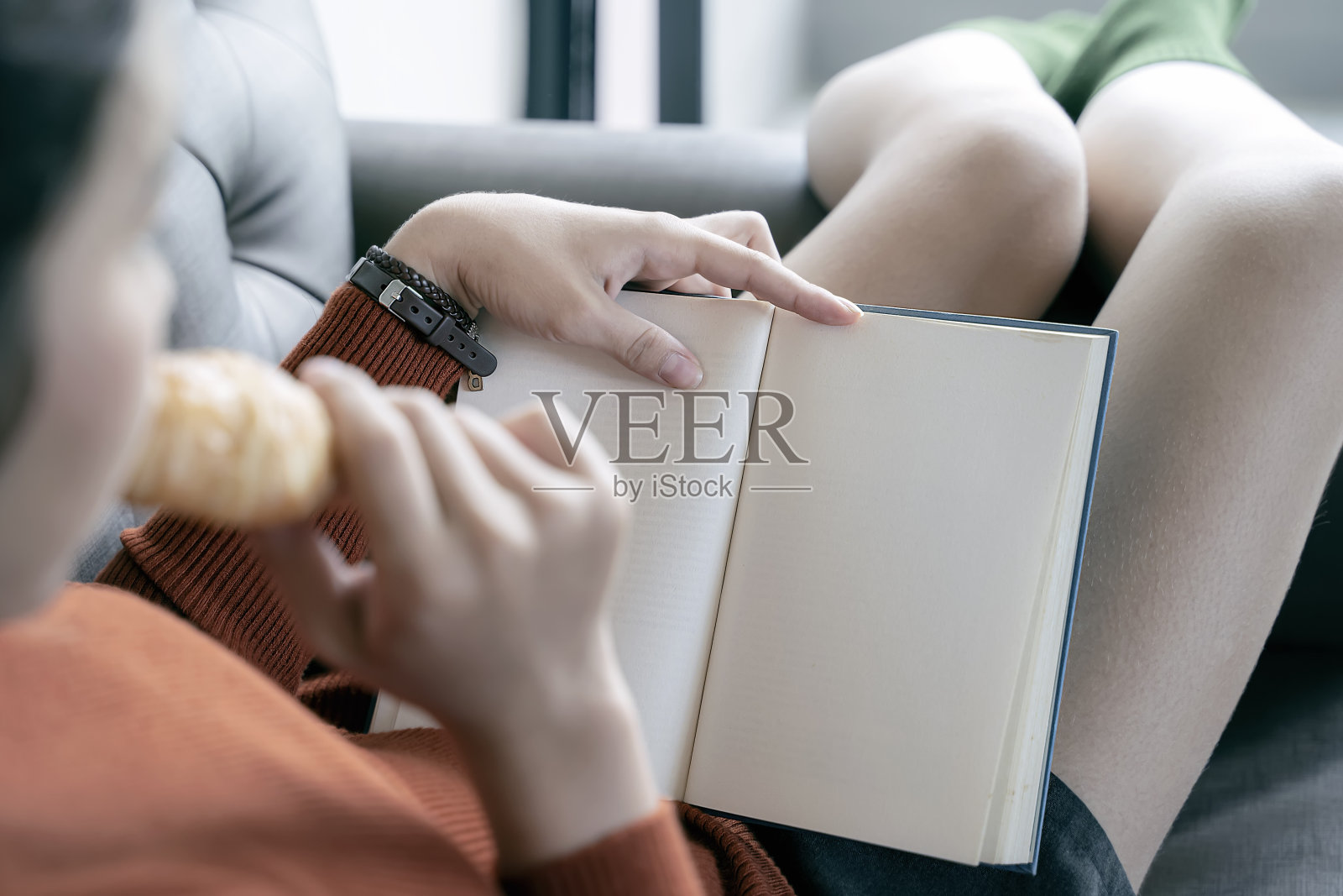 年轻女子躺在家里的沙发上看书。照片摄影图片